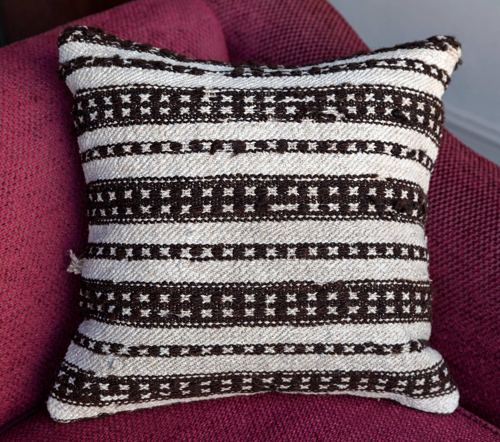 A handmade cushion covered with an antique Turkish rug with trim detailing, backed with a handwoven wool and hemp vintage fabric with a decorative stripe and a hand-embroidered HOWE logo.