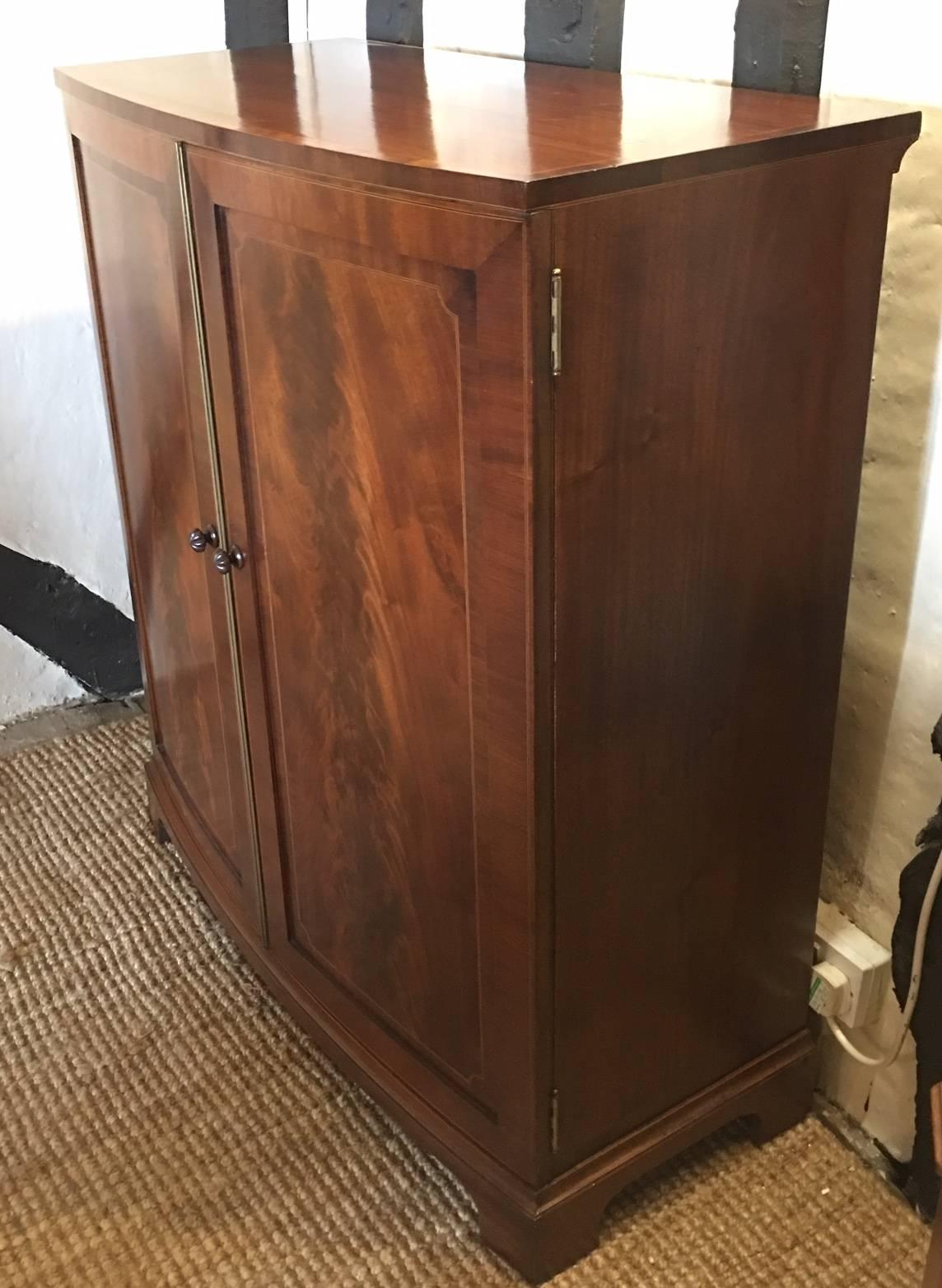 An Edwardian flame mahogany and inlaid bow front cabinet, circa 1900
Opening to reveal a shelved interior, raised on bracket feet.
Measure: (H 106.5cm x D 44.5cm x W 91cm).
 