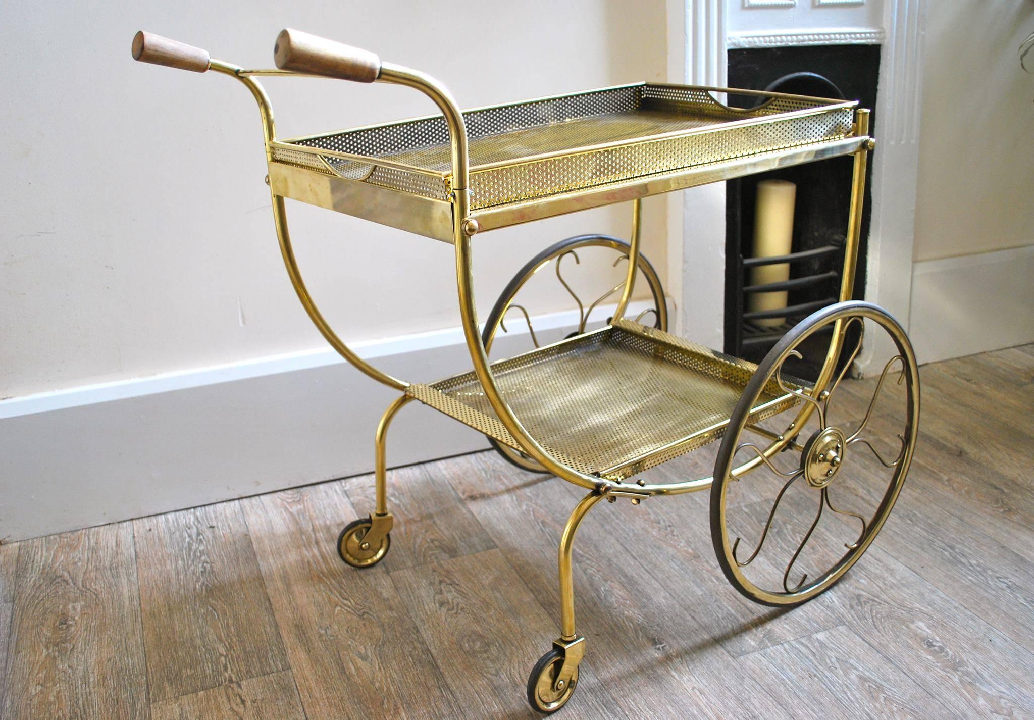 An elegant drinks trolley by Firma Scenka Tenn, Sweden. Original wooden handles and a curved body, two perforated removable brass trays. The exaggeretated front wheel with stylized spokes. Newly professionally polished brass gives luxurious looks.