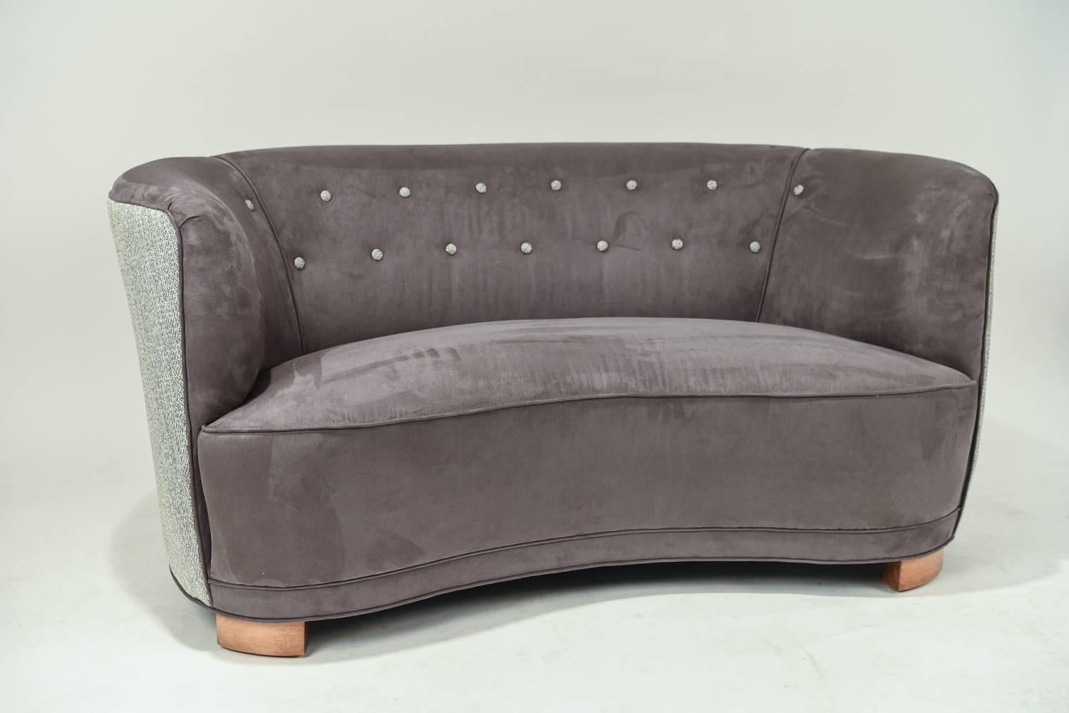 This Danish banana sofa or loveseat seats two people with ease. From the Art Deco period, this sofa originates circa 1940s, but the design remains popular today. This sofa sits upon short wooden feet, which allows for the body of the sofa to be the