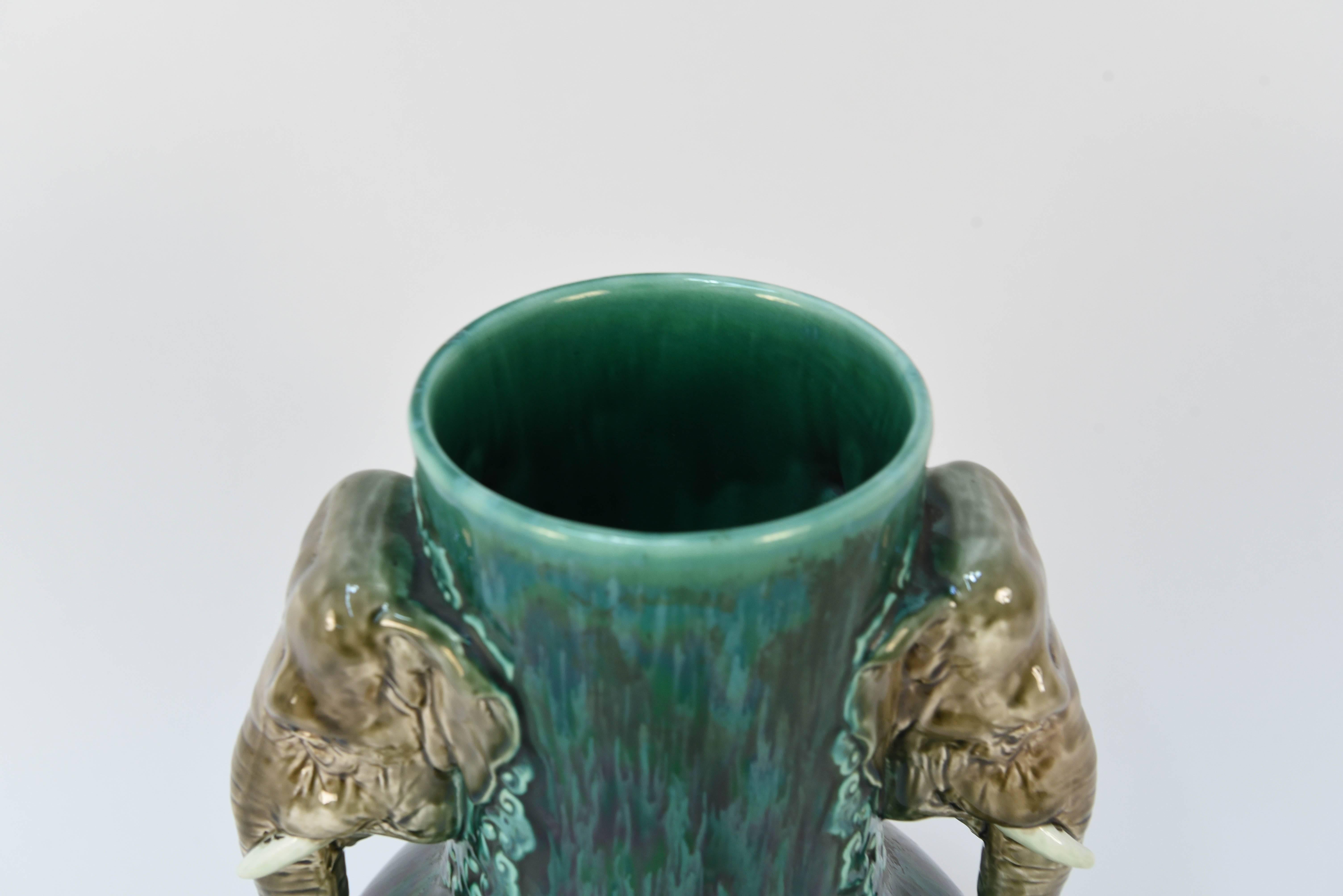 Questo vaso in ceramica presenta teste di elefante come manici e un bellissimo corpo in smalto verde. Un design delizioso che può essere utilizzato come elemento decorativo o per contenere dei fiori.
