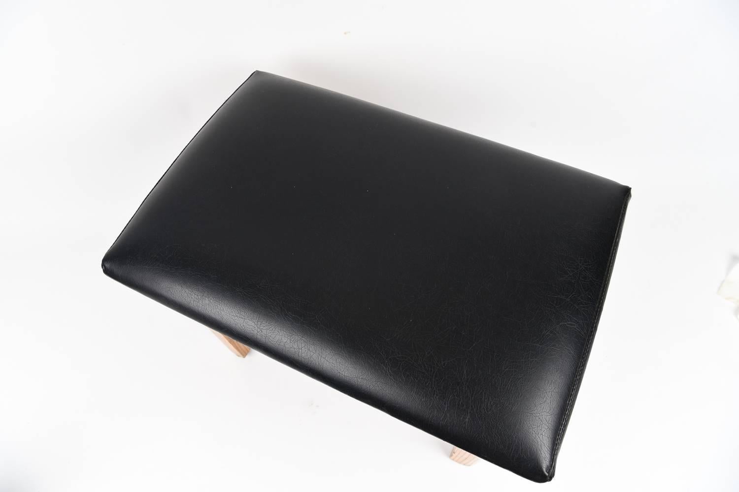 A beautiful stool or ottoman with black leather upholstery.