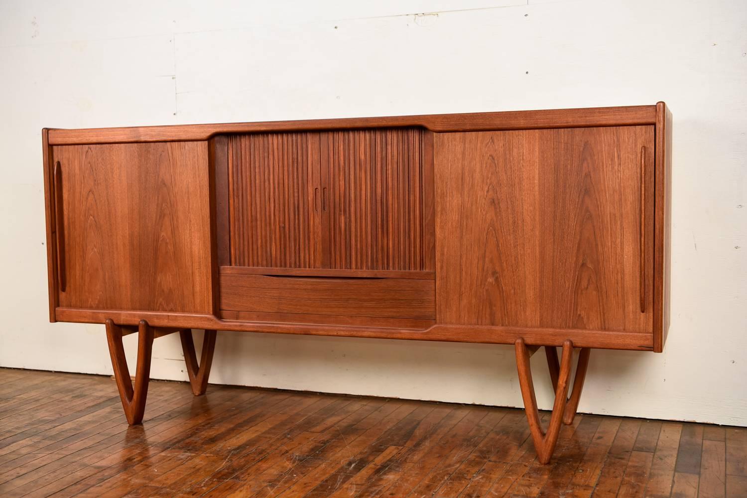Kurt Ostervig designed this beautiful Danish teak sideboard, circa 1960s. Has a wonderful form from the sliding door details, down to the triangular feet. The middle cabinet opens to a mirrored bar cabinet.