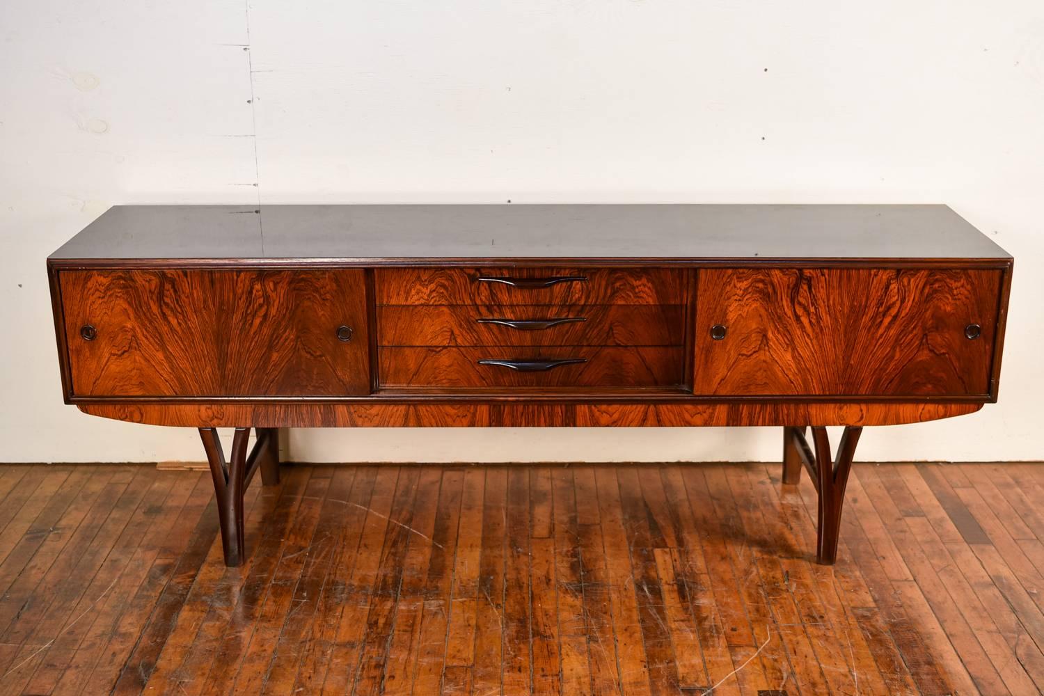 A stunning Danish midcentury sideboard in rosewood, featuring a black laminate top. The piece has a sliding door on either side with petite circular handles, and three stacked drawers in the centre with elegant handles. The legs of this piece are