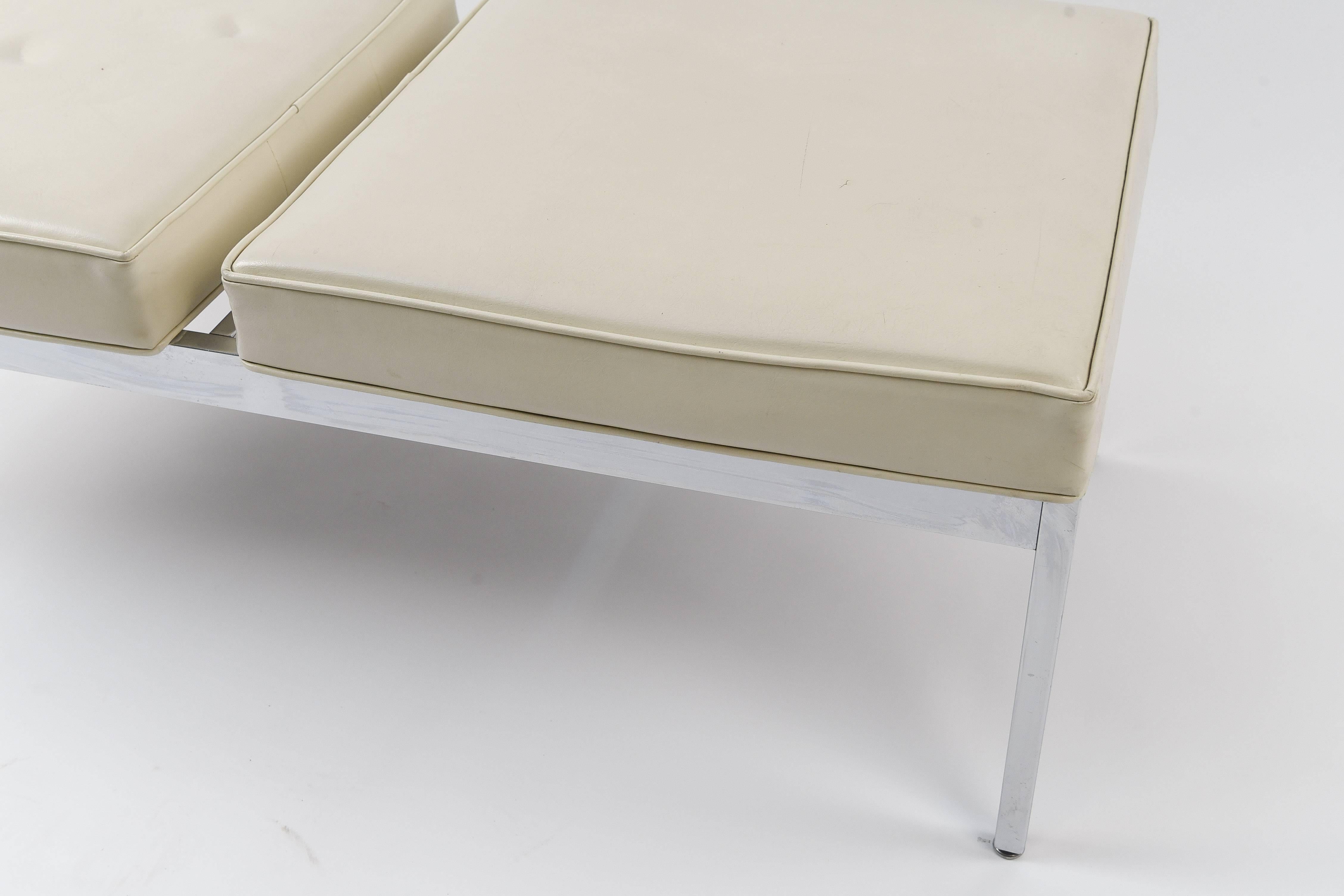 A two-seat midcentury bench on a chrome base featuring seats upholstered in vinyl. Has a sleek modern appeal. The divided seats are an interesting element.