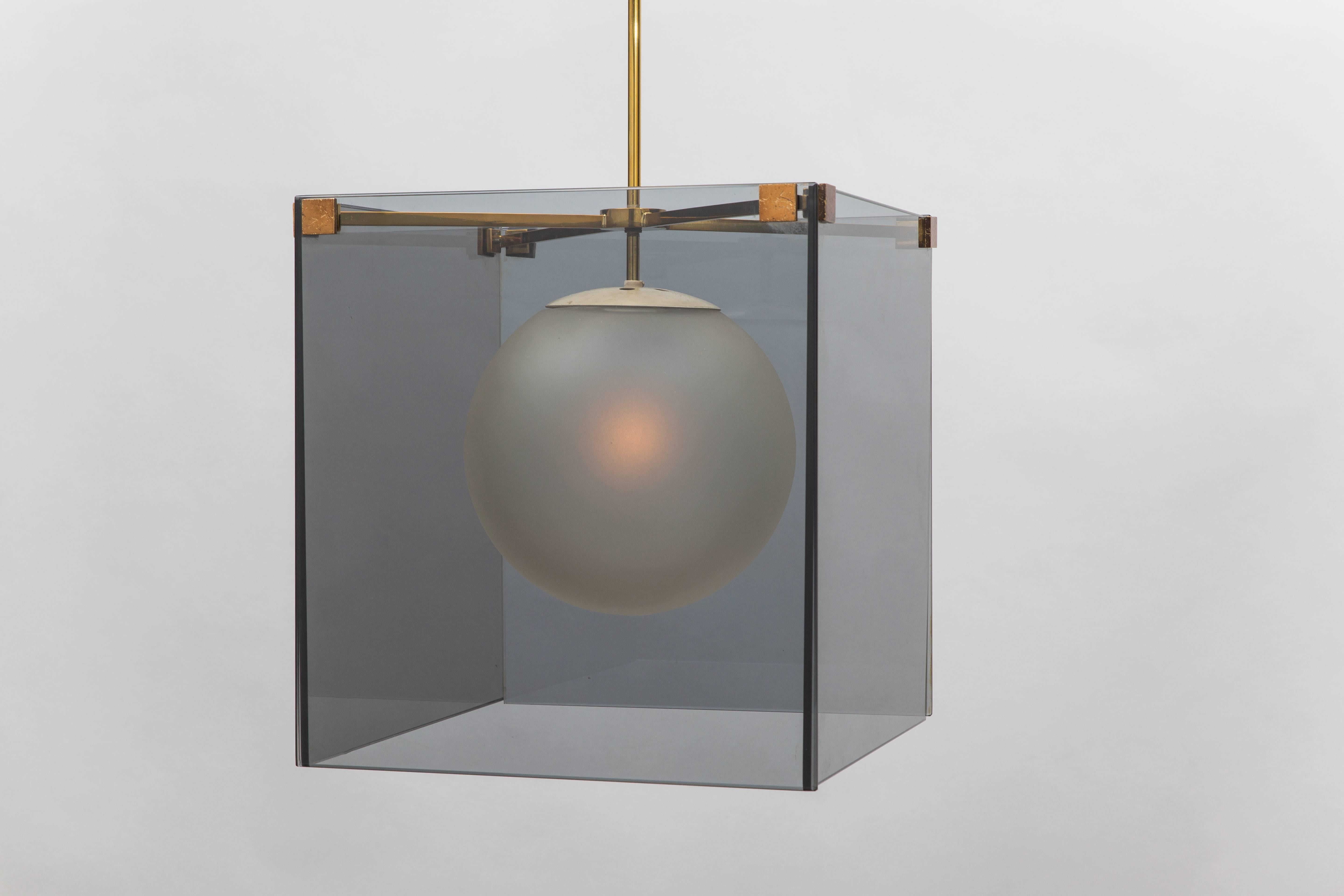 Max Ingrand for Fontana Arte rare chandelier composed of smoked glass plates suspended from gilt lacquer tubular brass frame, brass fittings and matching box canopy, and frosted glass globe hung on painted metal structure, Italy, circa 1965.  
This