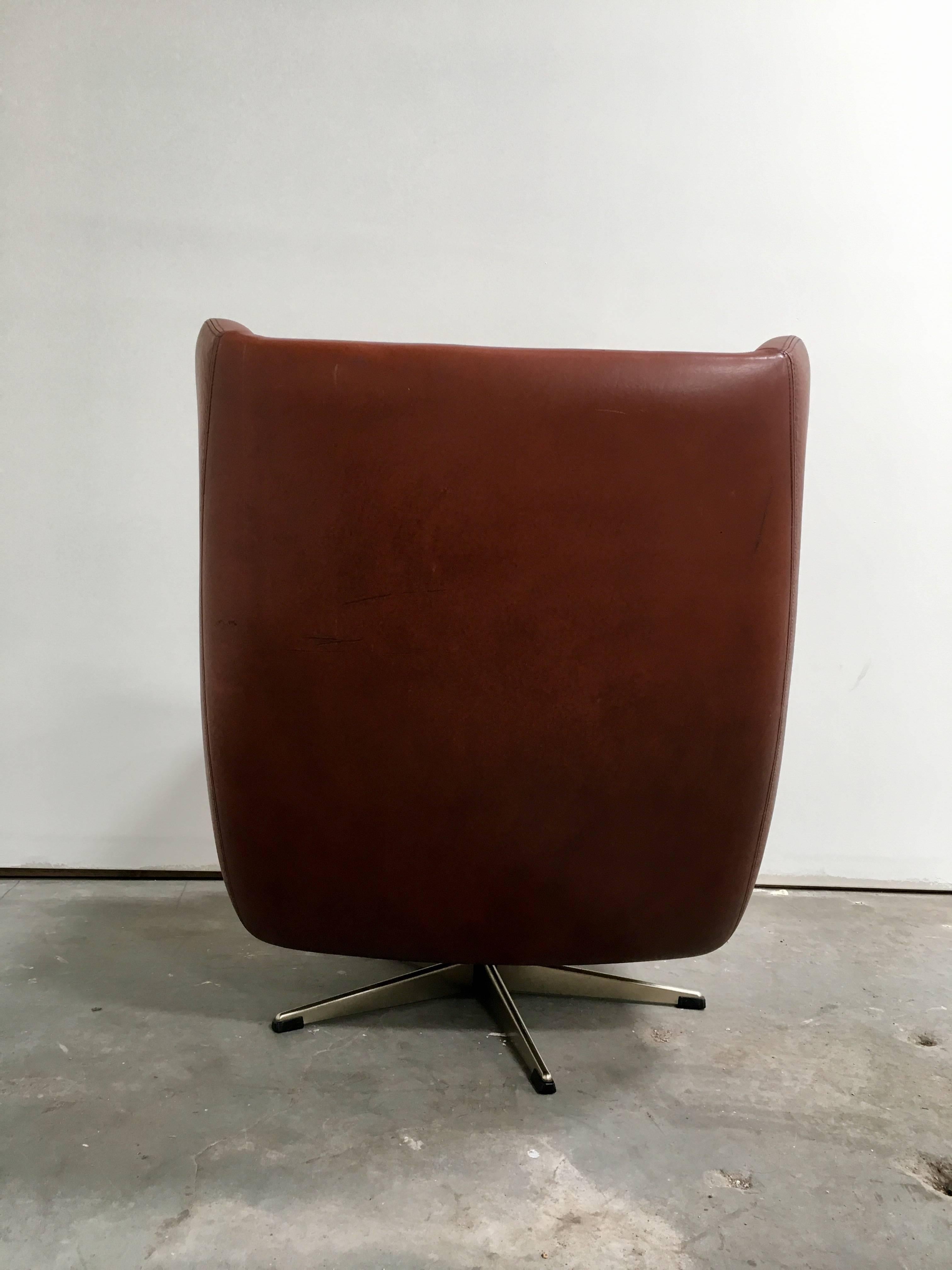 Vintage Danish Modern swivel chair in original brown leather upholstery. Two tufted back cushions and one tufted seat cushion, uniquely angular arm rests, and chrome metal base. 20