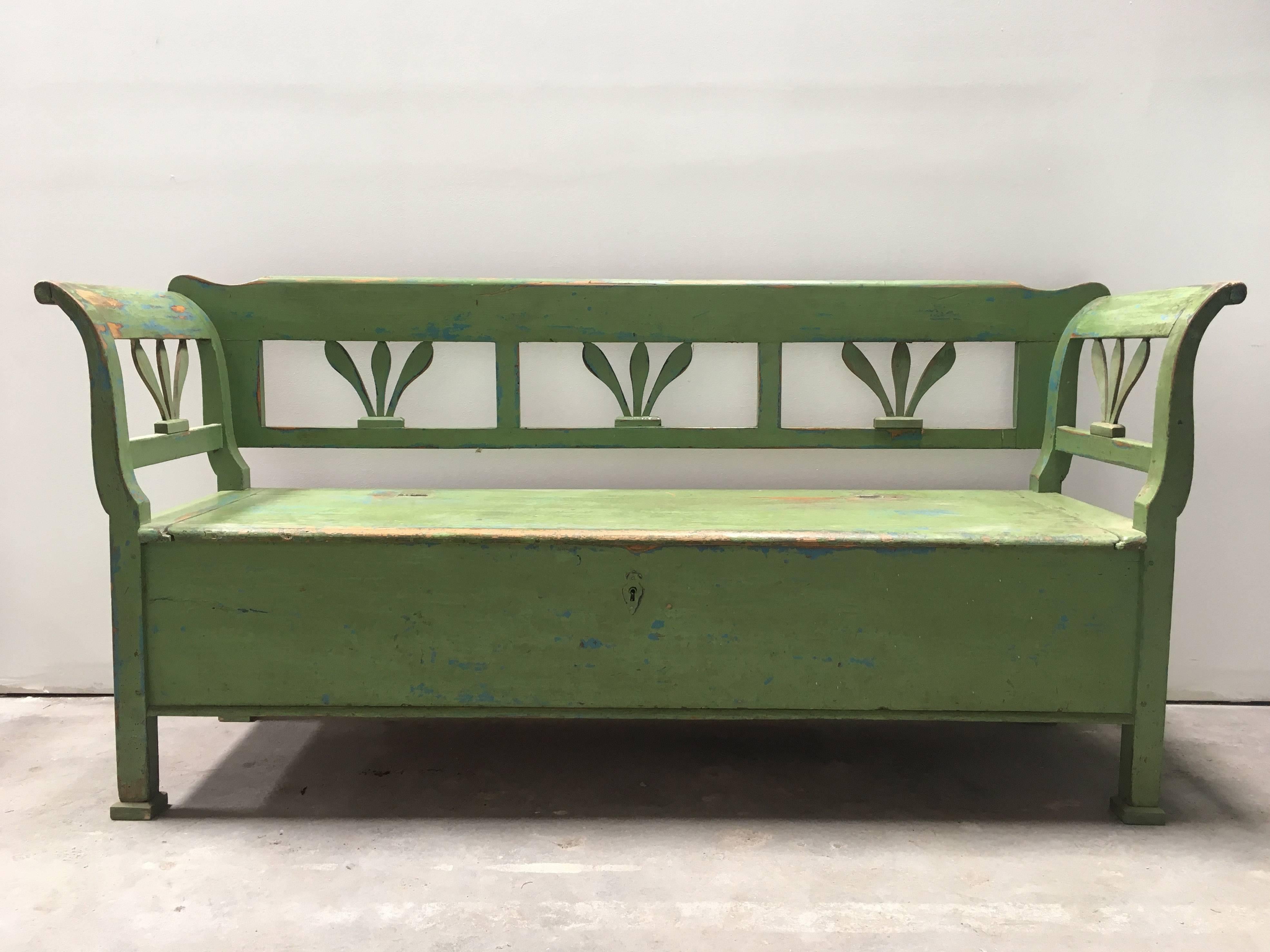 This antique bench Swedish bench is painted a vibrant pear green which is worn to rustic perfection. Curvaceous armrests, decorative floral carvings, and a seat that opens up to two storage compartments. The interior and exterior of this item are in