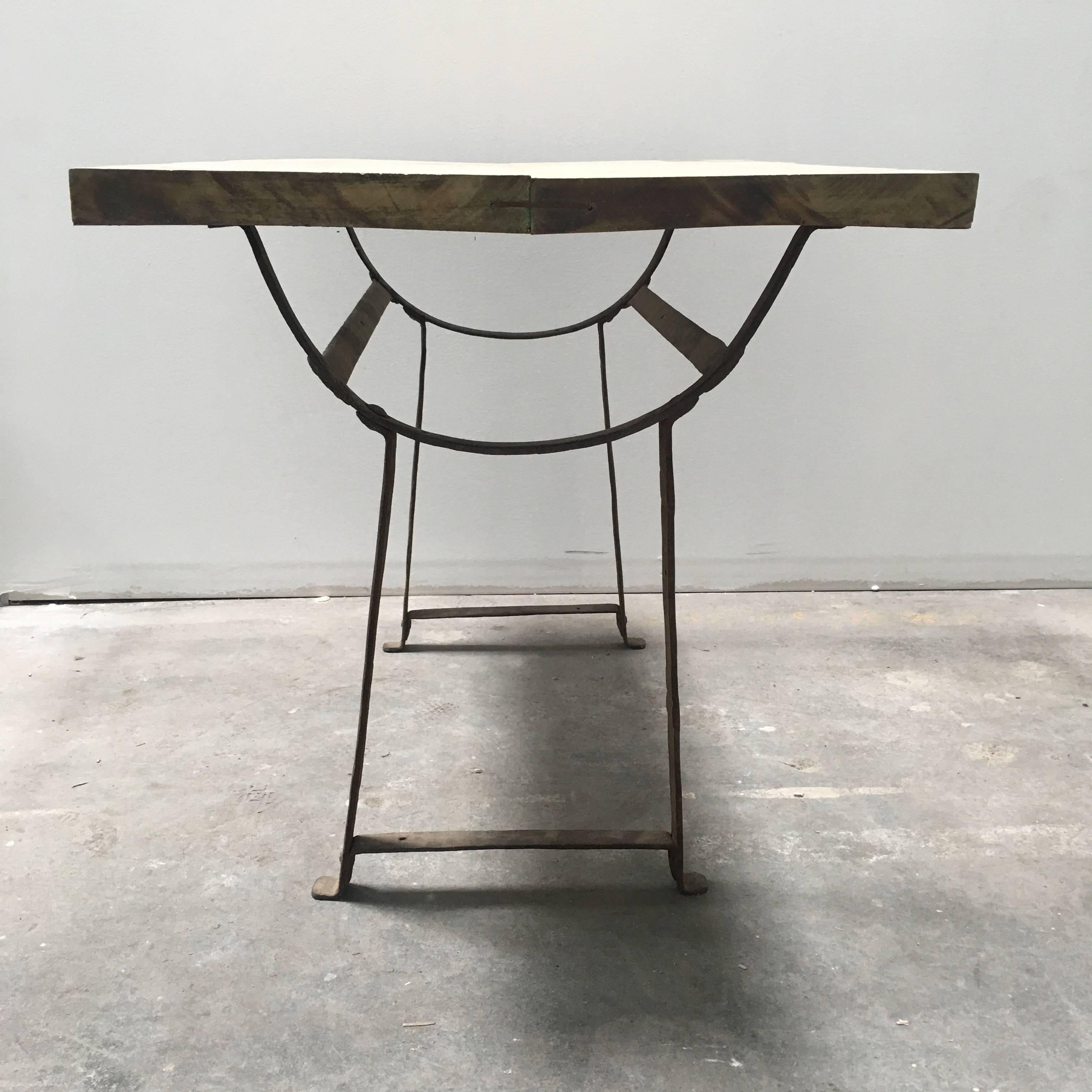 European trestle farm table from the 1800s with a metal base and a light wood tabletop.