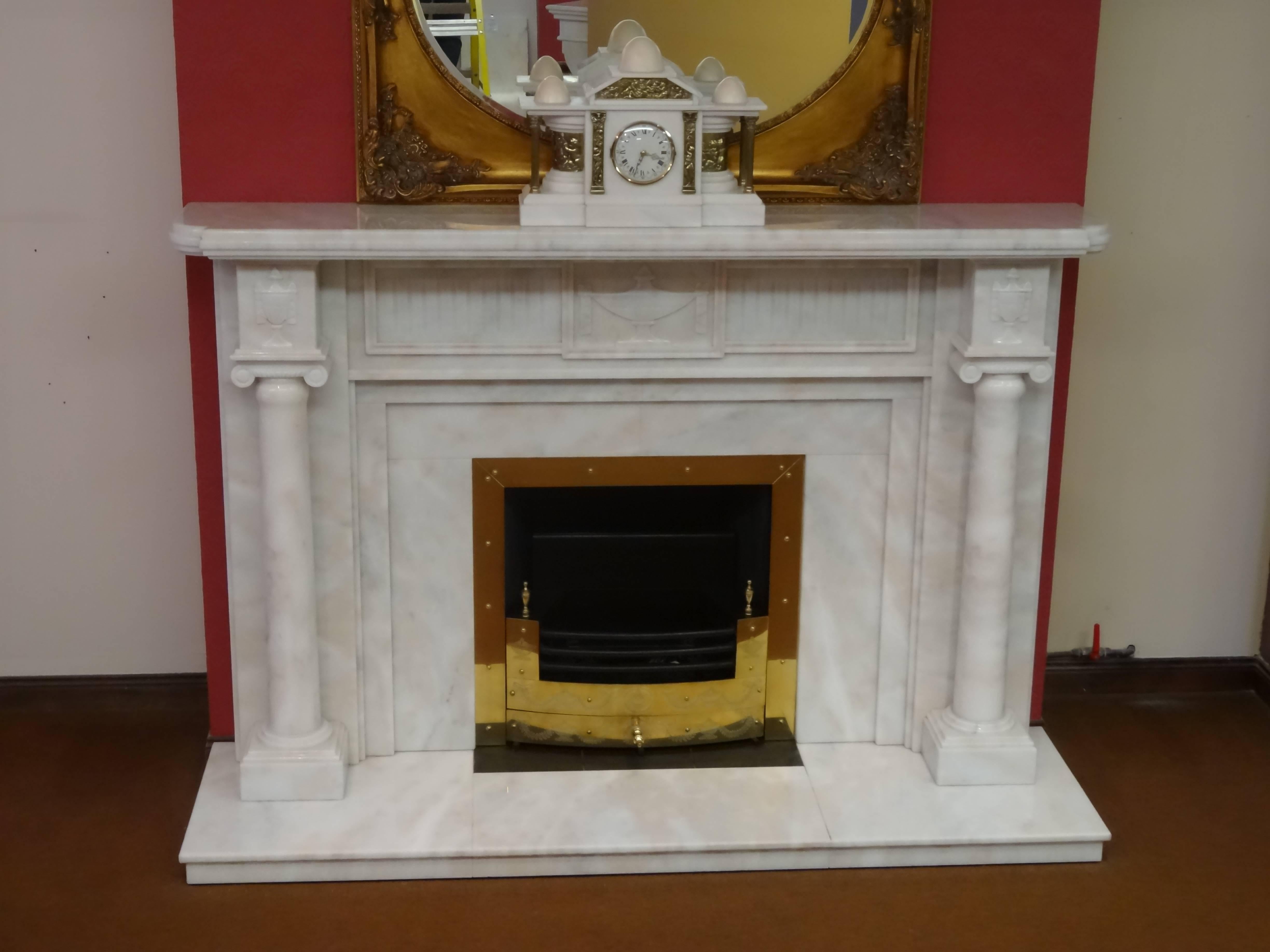 We created this fireplace from polished Greek Marble. It features carved Adam's Urn to the frieze, tapered columns with caps. The fireplace comprises matching marble hearth and insert with a built in brass trim and a removable engraved brass fire