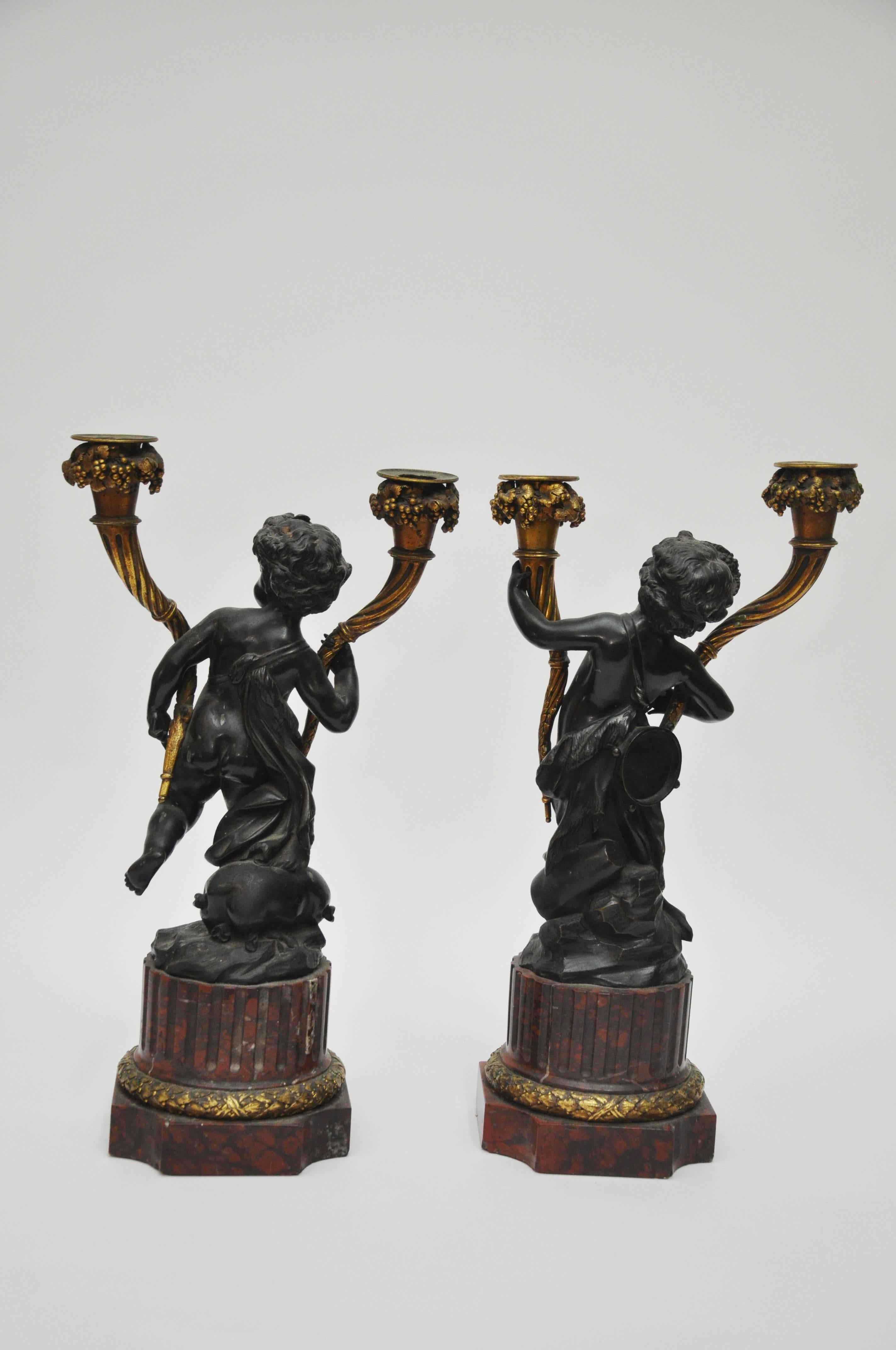 A very fine pair of French 19th century Louis xvi style patinated and gilt bronze figural two-light candelabra after a model by Claude-Michel Clodion (French, 1738-1814), modeled as cherubs, each holding a gilt bronze, two-light candle holder, and