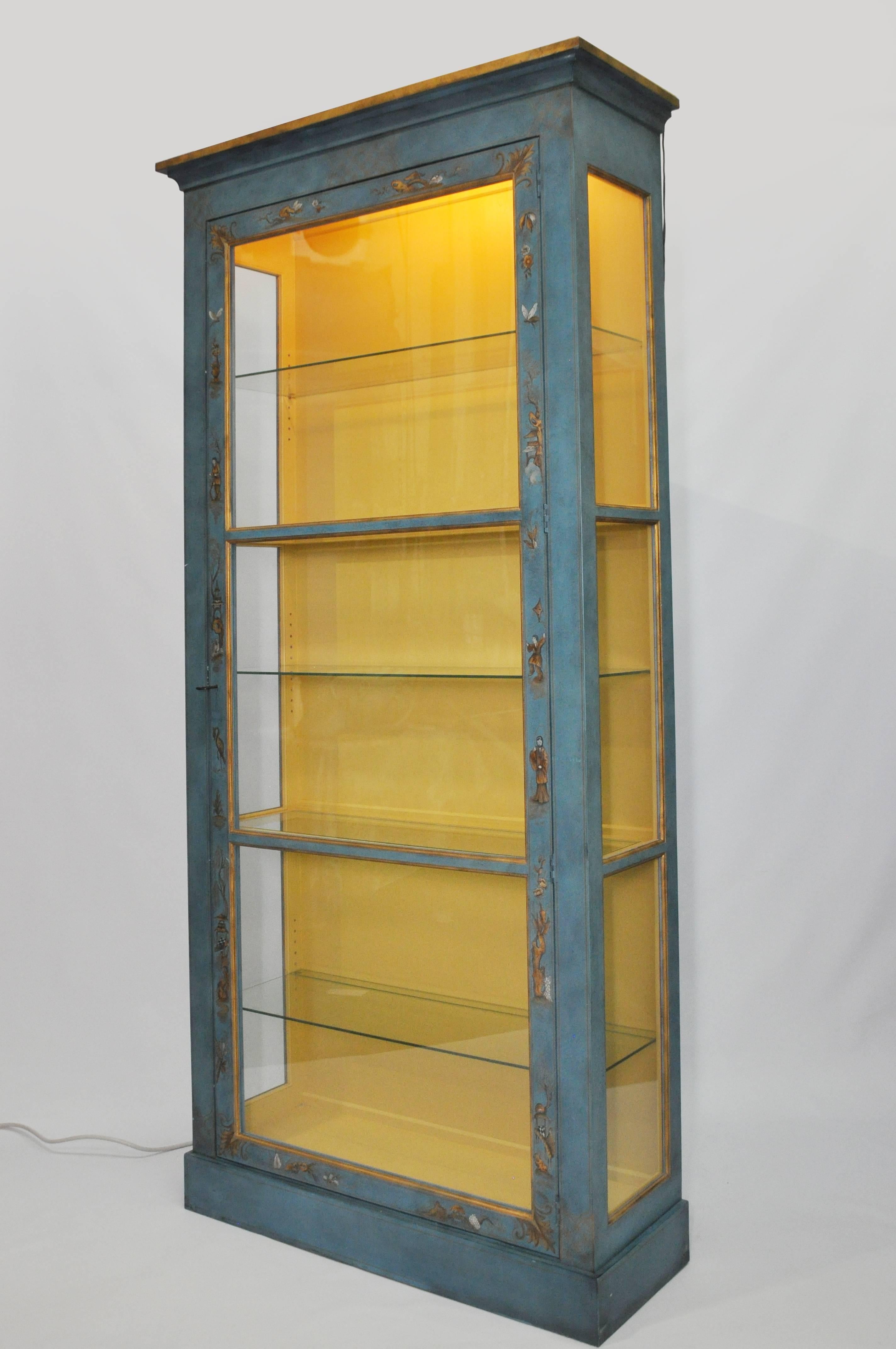 Tall, elegant display cabinet with a custom mottled blue painted finish with hand-painted chinoiserie motifs. The illuminated interior is a rich, egg-yolk yellow. Two stationary wood-framed glass shelves for structural stability; and three