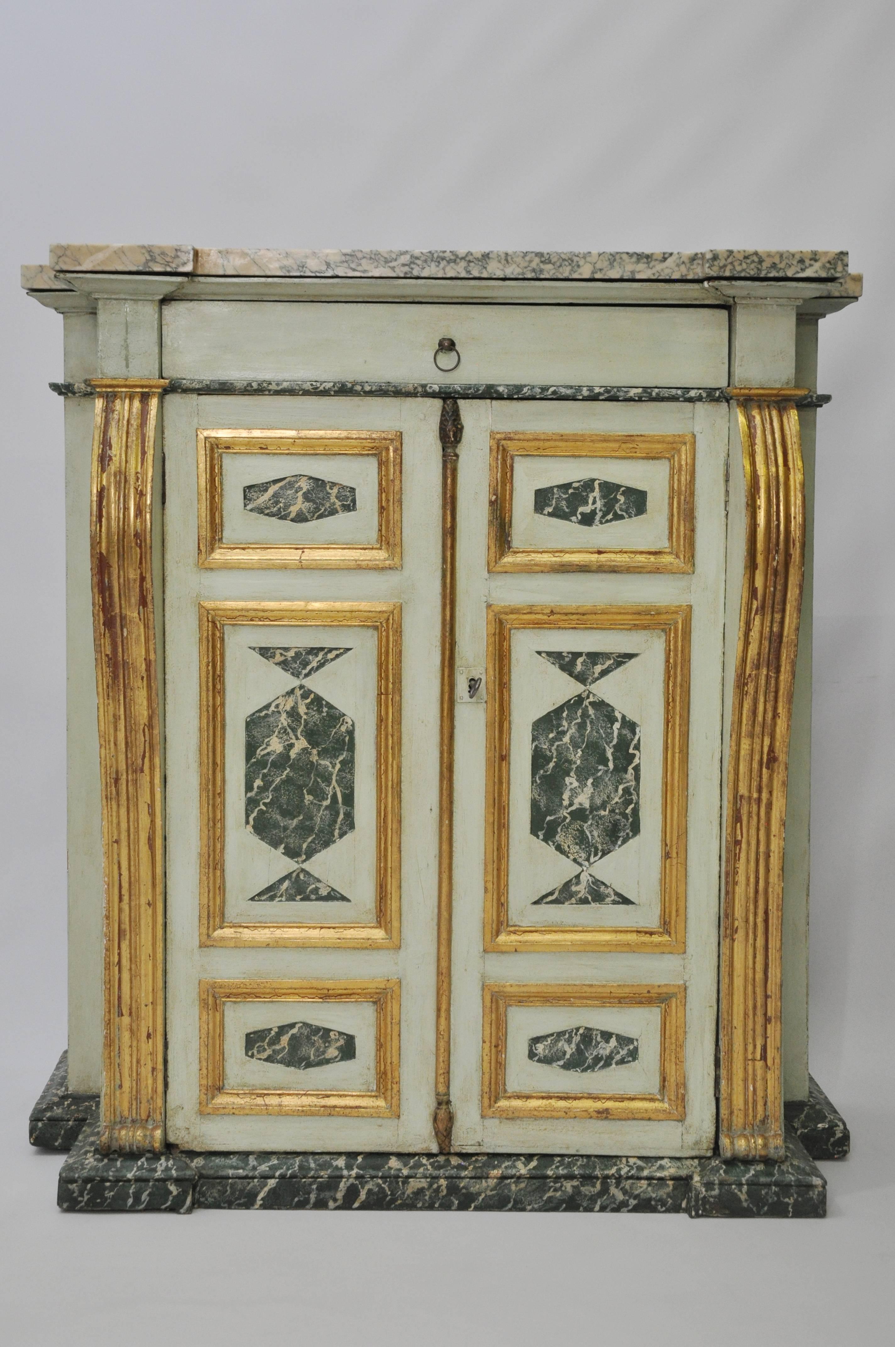 Elegant painted Provincial Italian cabinet with heavy marble top. Pale green dragged finish over pine, with panels of faux-painted marble. Gilt framing and accents. A single drawer over two cabinet doors that open to reveal interior storage. There