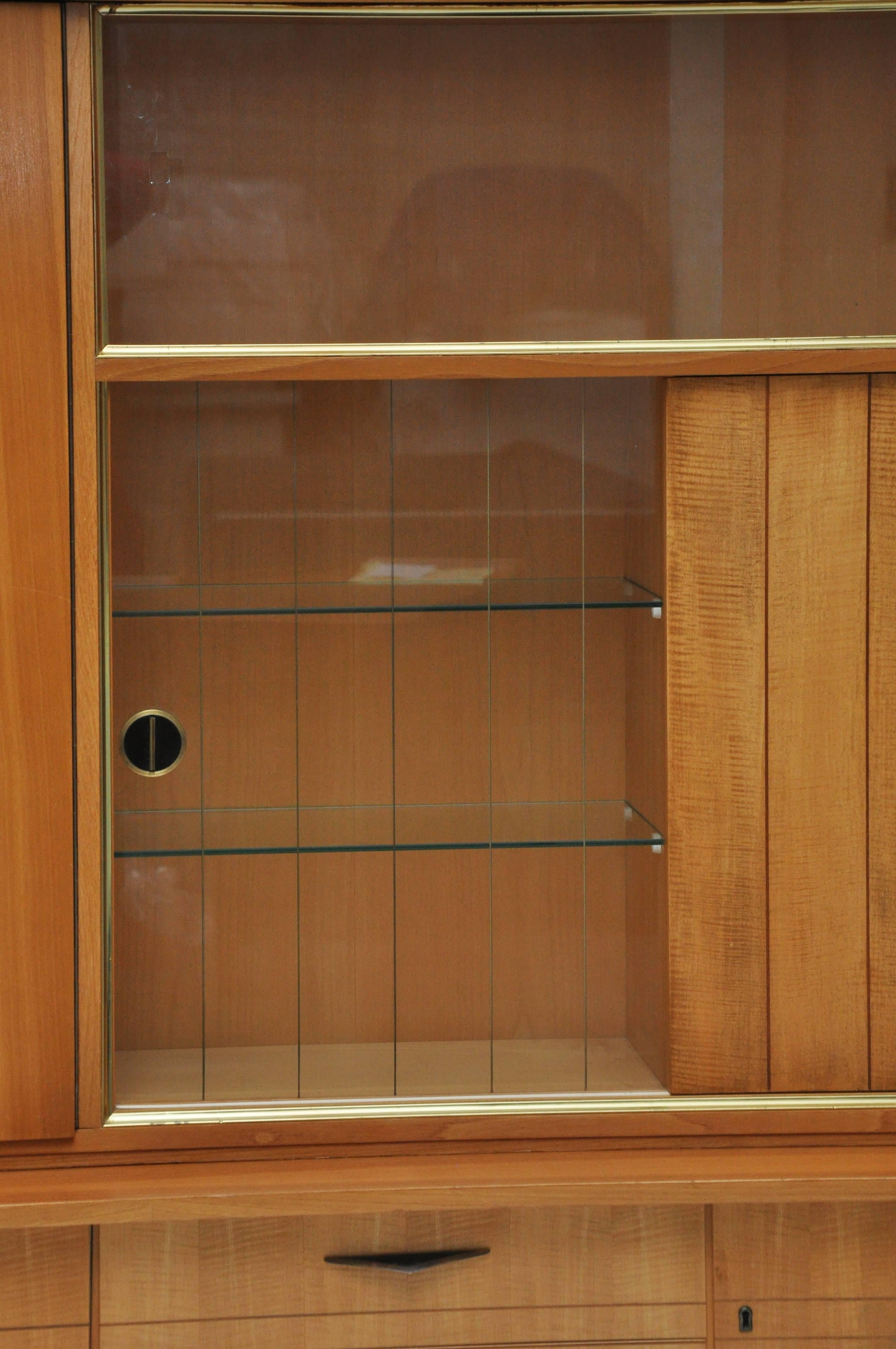 This midcentury piece was manufactured in Germany in the 1950s. 

The top portion sits on the bottom and is in two separate pieces.  There is a locking shelf section and storage unit with a glass door and shelves.  Also, it has an etched striped