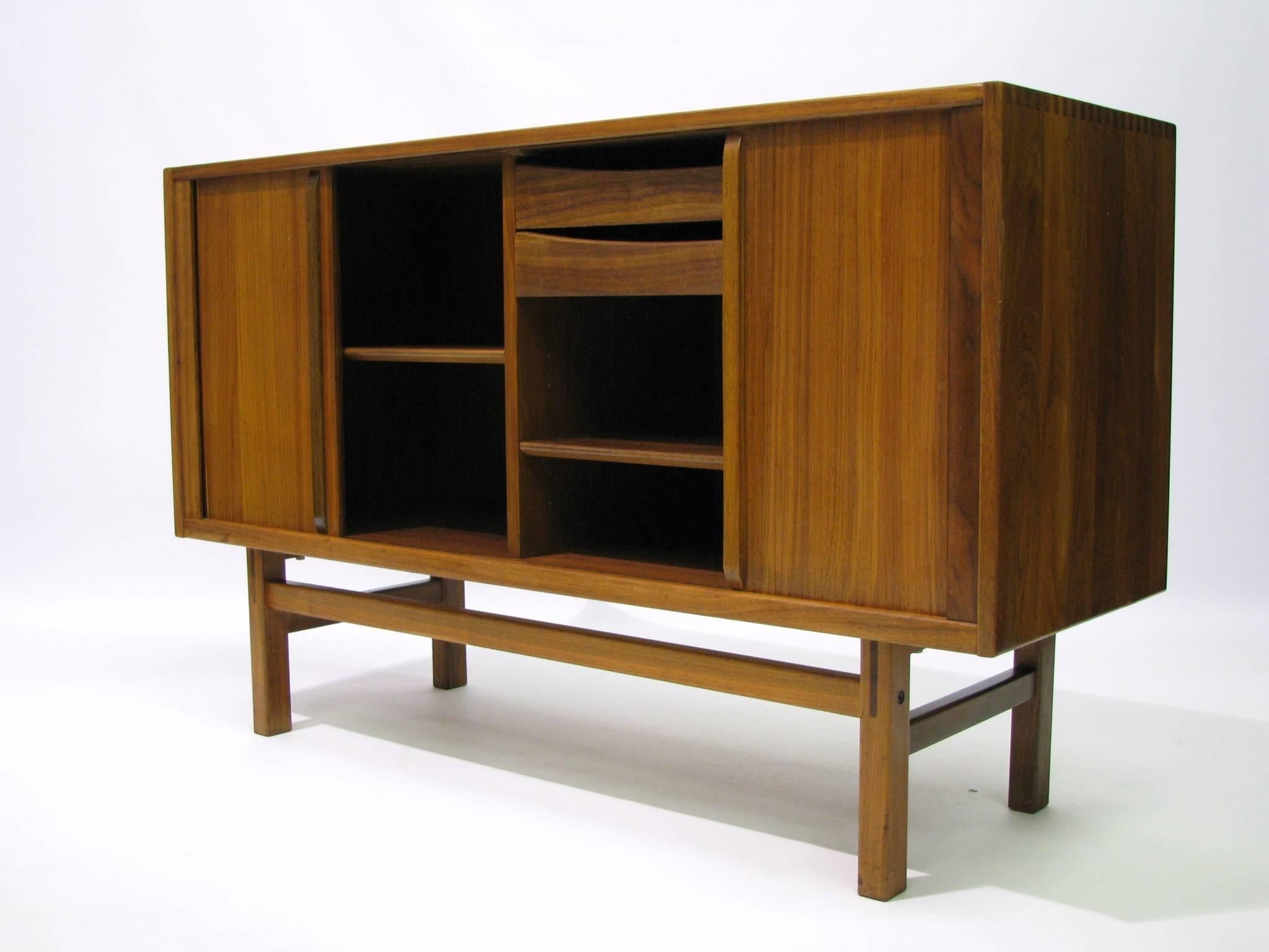 Teak sideboard designed by Nils Jönsson for the Swedish firm Troeds Bjärnum in the 1960s. Attractively grained wood with exposed dovetails on the top corners. Tambour doors reveal an adjustable shelf on the left, and two drawers, one for flatware