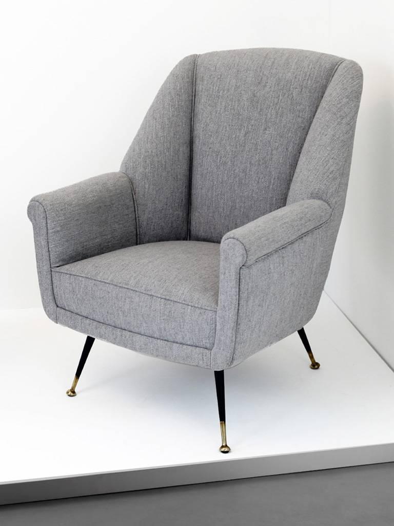 A pair of Italian lounge chairs newly upholstered in a sophisticated, light grey, woollen fabric. These extremely comfortable chairs sit on elegant, brass splayed legs which are both black lacquered and polished at their feet.
         