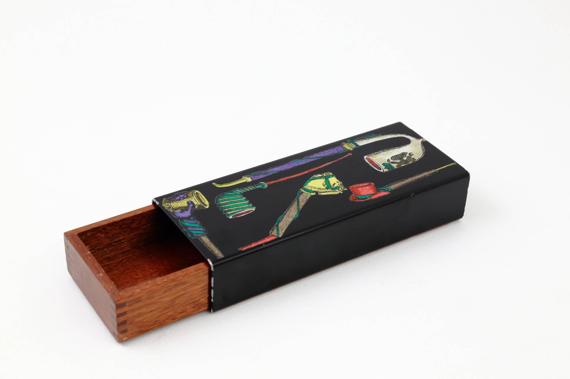 A vintage trinket box by Piero Fornasetti, circa 1950. The lacquered, metal exterior features colored transfers with ‘pipe’ motif, whilst the wooden mahogany insert has beautifully crafted 'dovetail' joints. An exquisite accessory or table piece