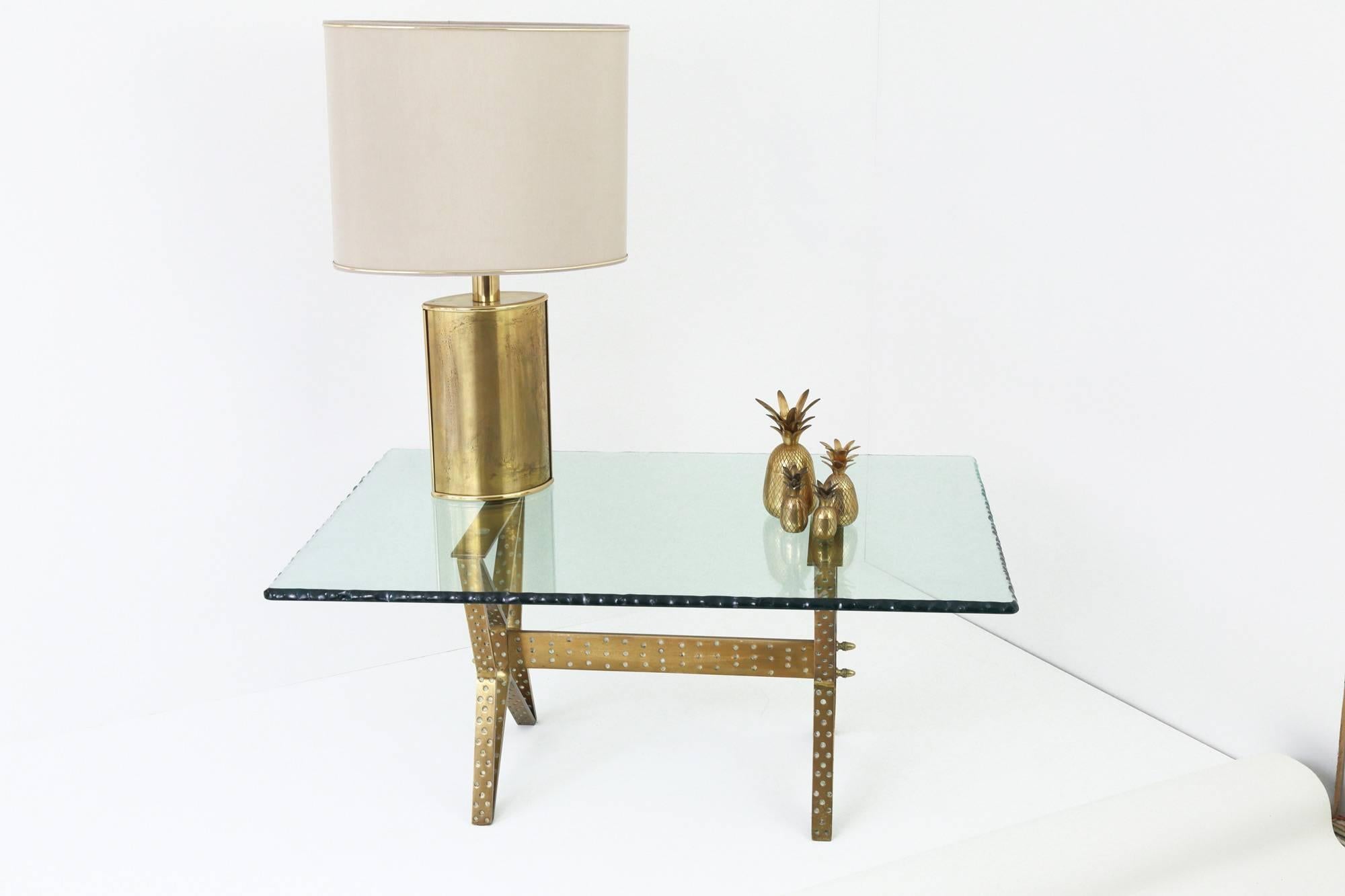 A hammered, solid brass coffee table with a beautiful, green, ‘scalpellato’ glass top. The two, ‘X’ shaped, table base supports are linked together with a horizontal, brass crossbar that feature double finials at each end. The hand-chiselled glass
