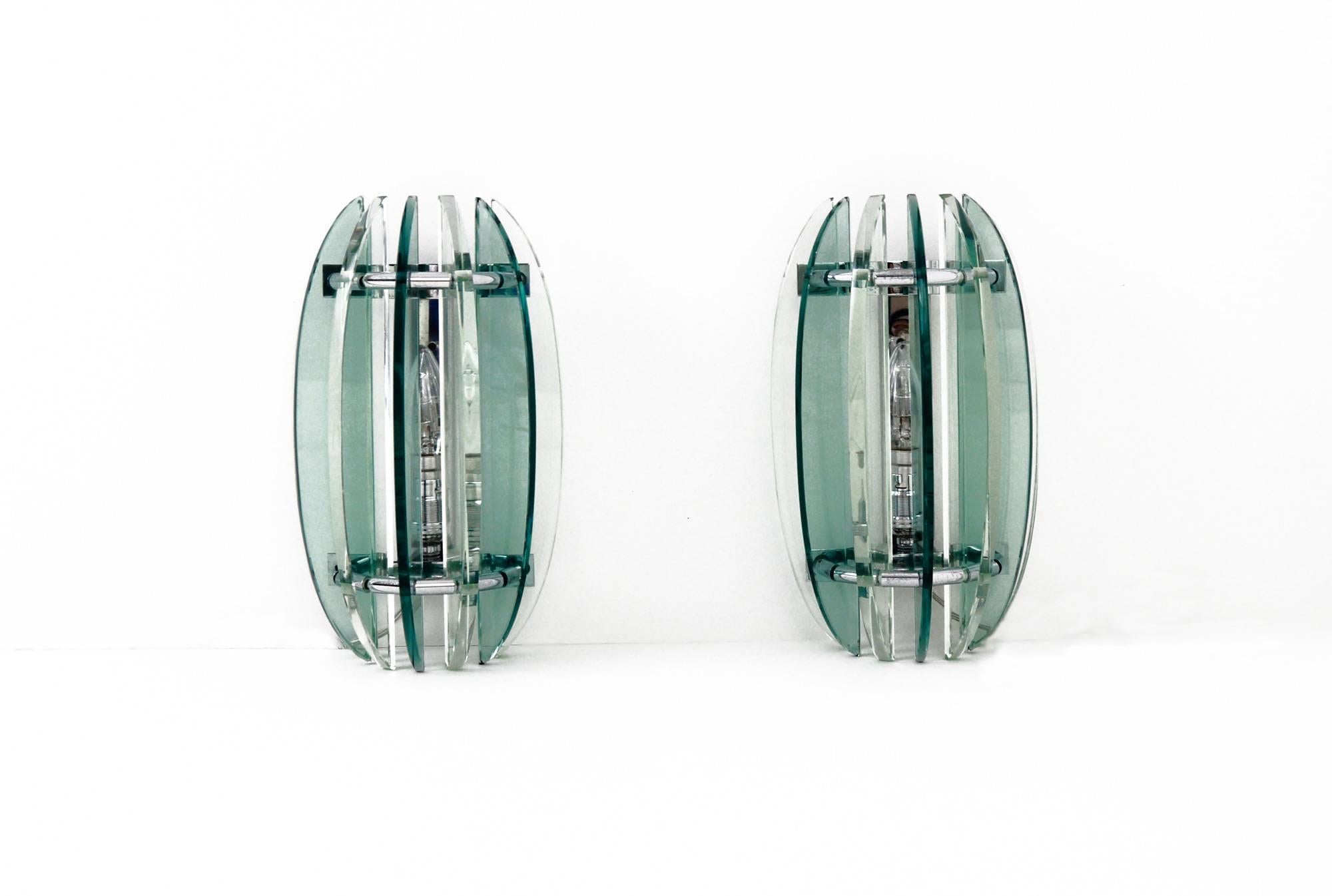 A pair of clear and green glass appliques from the Italian light company, Veca. Manufactured in the 1970s, the lights have seven, alternating, crescent shaped glass pieces and are attached to chrome body of the lamp in a semi-circular formation