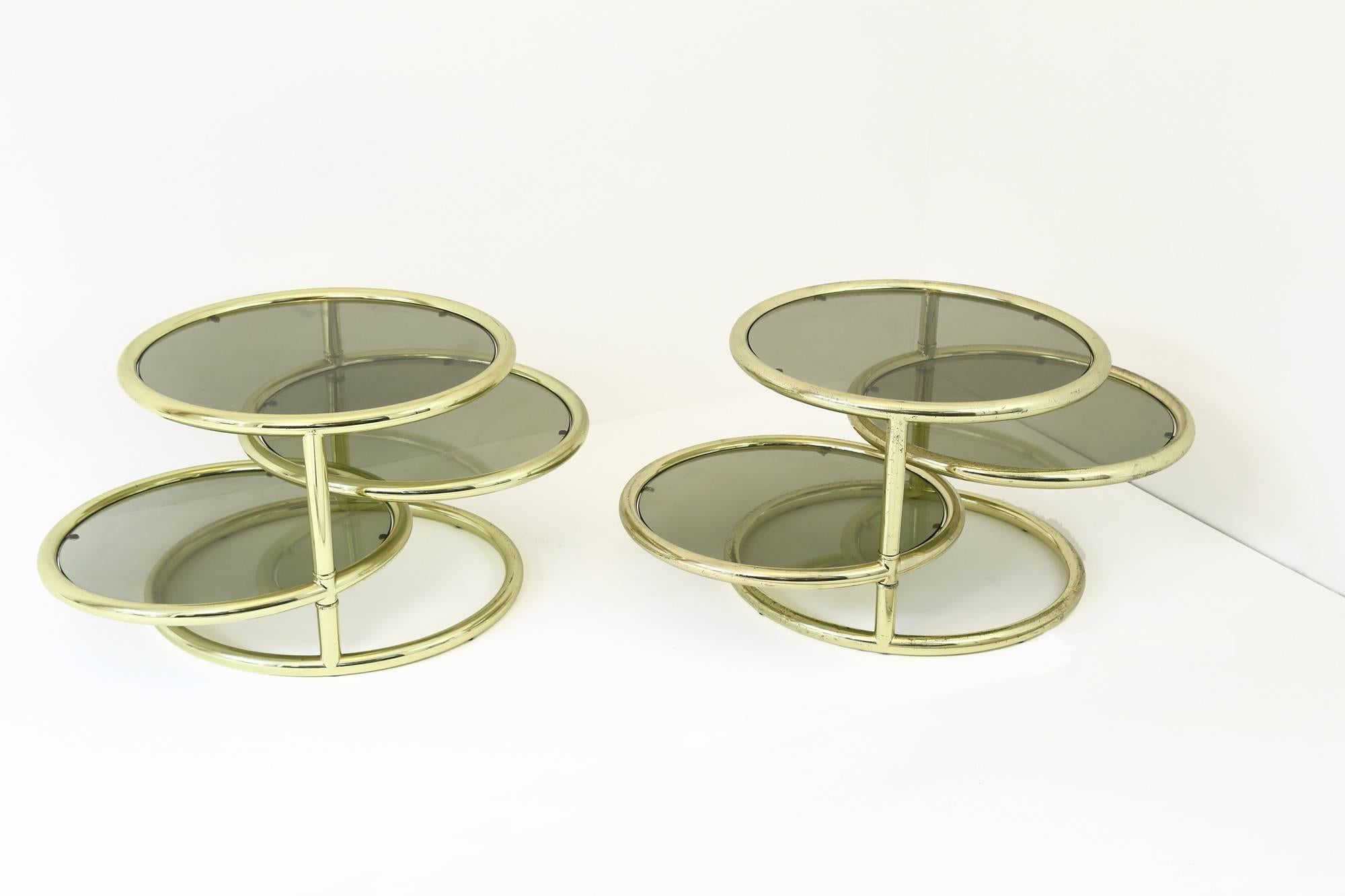 A pair of circular, coffee tables in the style of Milo Baughman. These tables are extremely versatile as the two central shelves are able to be rotated horizontally, providing a greater, more useable surface area, if so desired. The gold-lacquered,