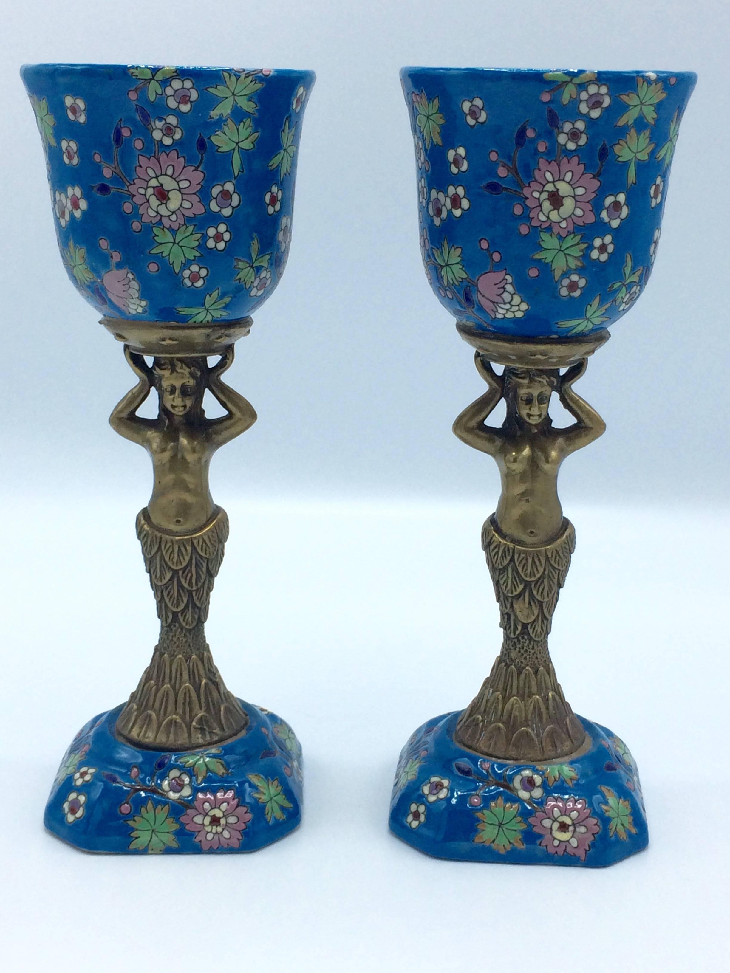For your consideration,

A colorful pair of Longwy chalices from France. These little vases or vessels dress up very nicely with a small low hanging plant.

They are two detailed brass mermaid figurines carrying a cup/chalice with the typical