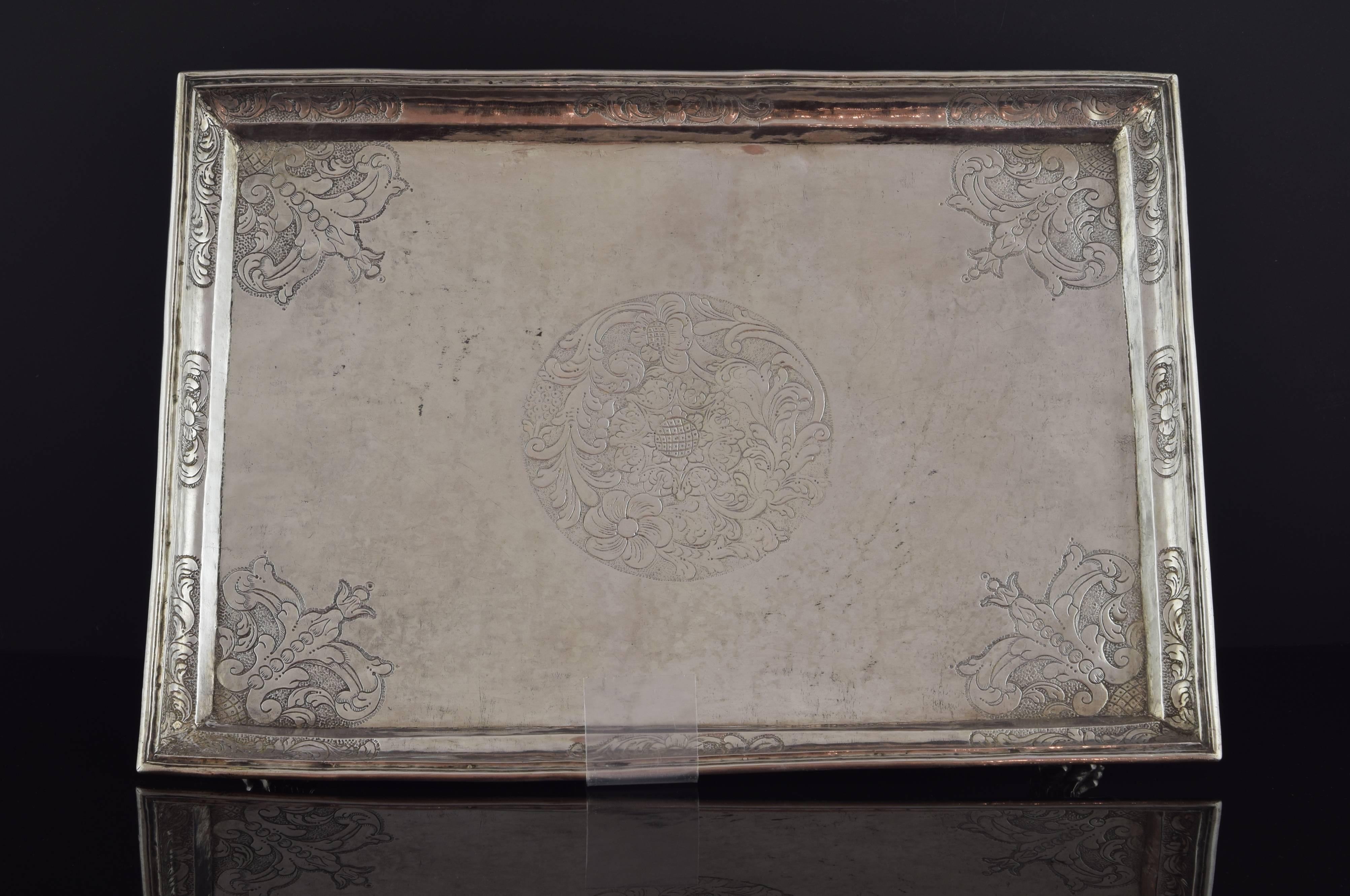 Rectangular solid silver tray raised over four beast claws, with remarkable detail on the skin, nails and anatomy. The upper part has a series of decorative elements engraved: in the center, a circular shape with plant and floral motifs; the corners