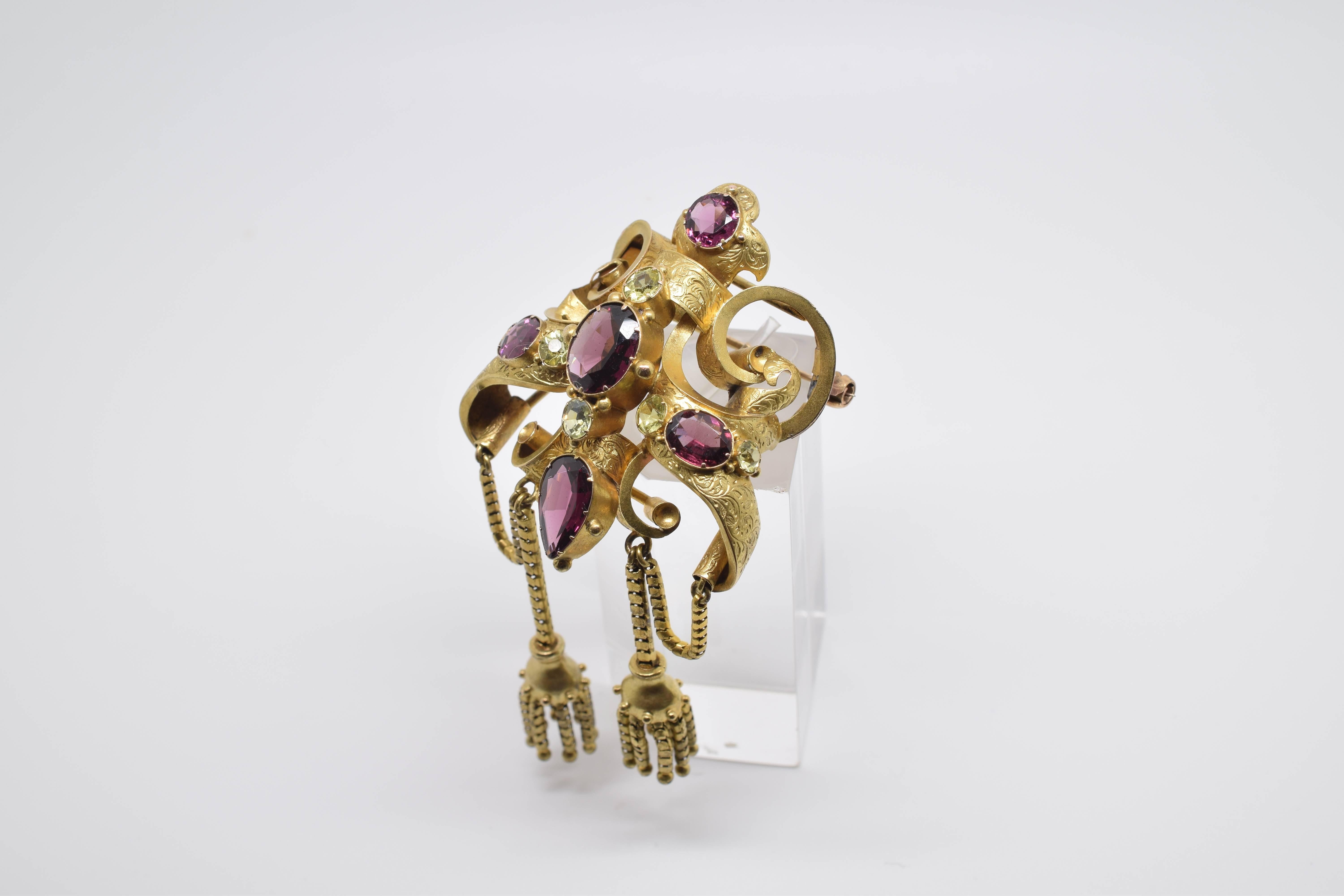 18-carat gold brooch with and ellegant symmetrical composition based on loops and scrolls with a fine decoration in high relief of vegetal elements with slight resemblance to neoclassic pieces. In the top, a circular faceted garnet is presented,