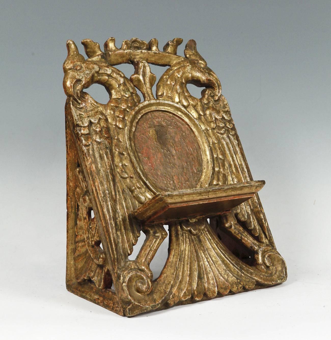 Mexican baroque ensemble entirely made of carved and gilded wood. Presents prismatic shape, with the front tilted to facilitate the support of the book. At the middle height of the front there is a flat, perimeter shaped bracket shaped like a