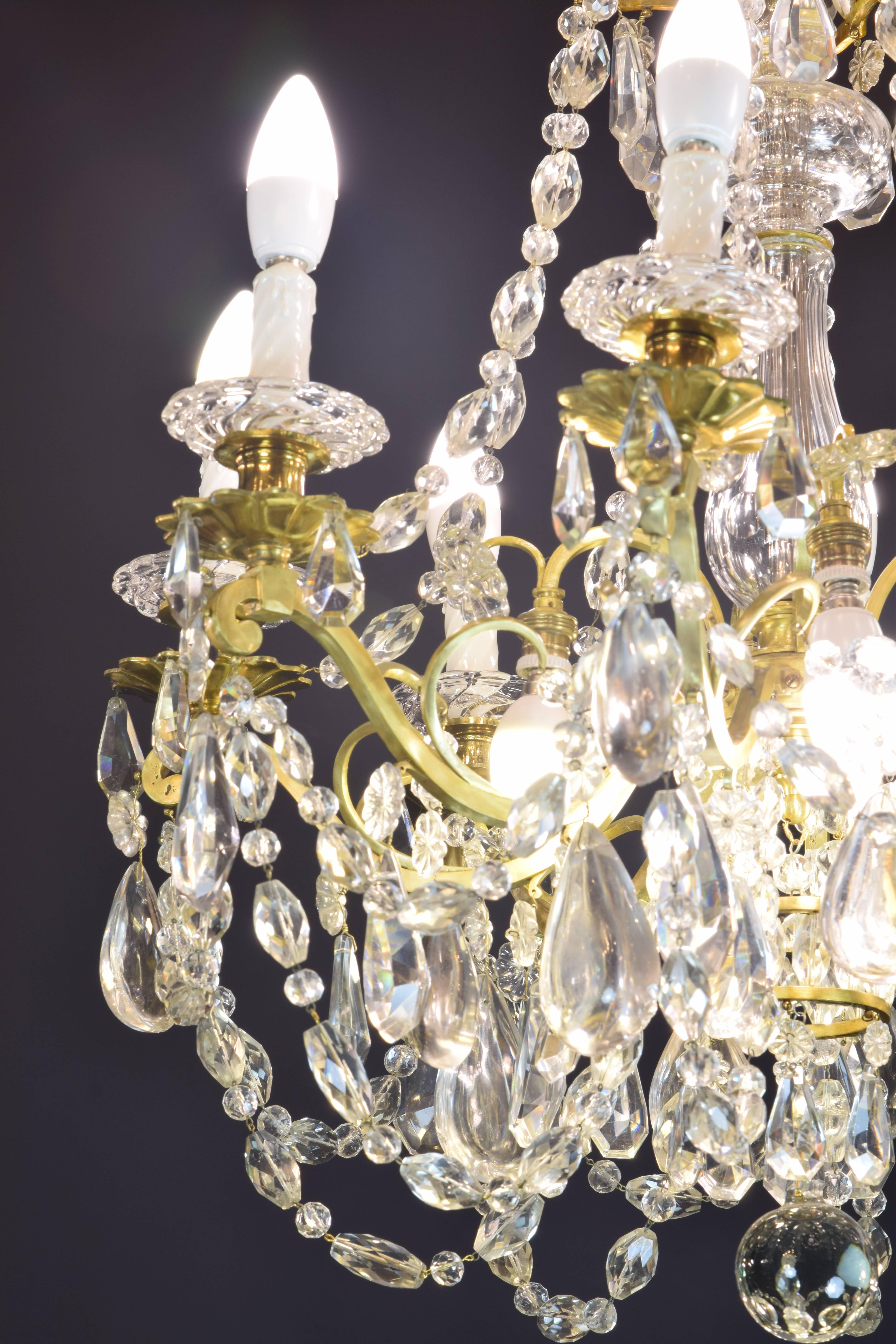 Baccarat signed chandelier. Glass and gilt bronze, 19th century.
Gilt bronze and transparent glass chandelier with eight lights. The upper part has a series of curved sticks from which hang some glass beads in various shapes (flower, tear). The