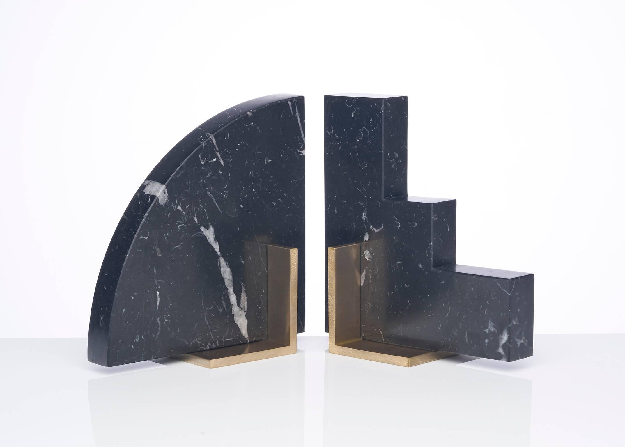 Meet Curvy and Steppy; the two individual bookends which as a pair are known as the Odd Couple bookends. 
Here shown in a honed Nero Marquinia marble and a brushed brass base.
Nero Marquinia marble from Spain is cut into two geometric shapes and