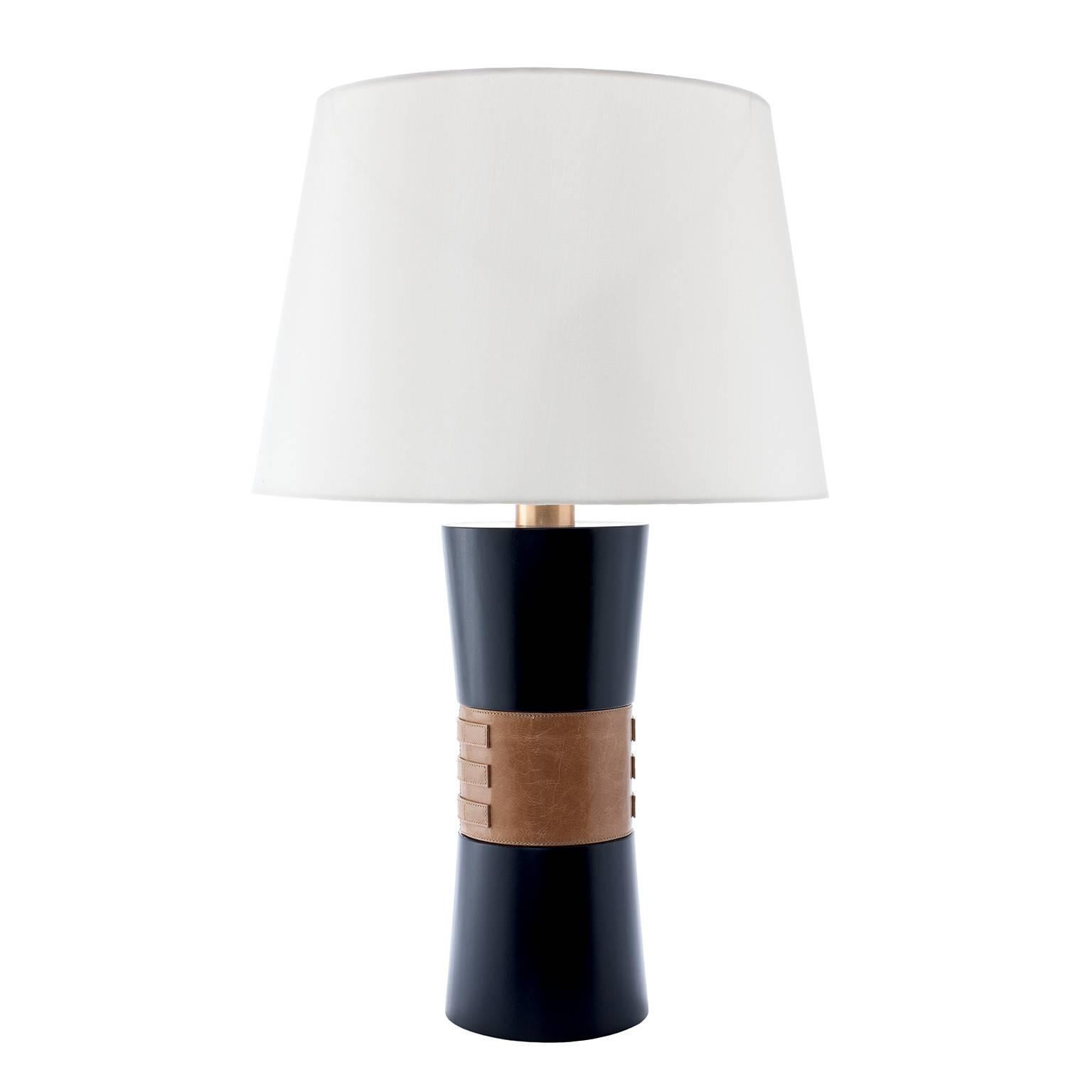 The Mina table lamp is made of solid turned wood and has a standout tailored detail in genuine leather with brass buckles at its centre. This lamp comes in various finishes and leathers as well as c.o.l. It is shown here in a midnight blue wood