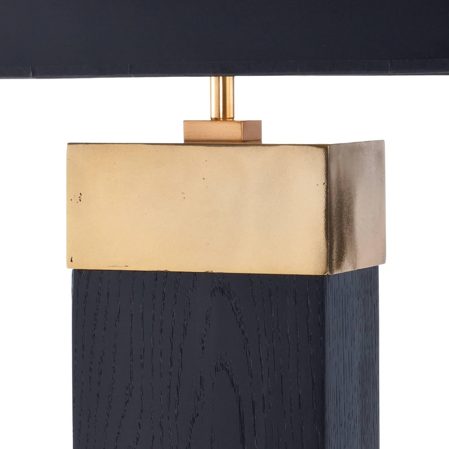 La lampe de table Tribeca est présentée ici dans une finition en chêne massif ébénisé avec un plateau et une section inférieure en bronze moulé finis en patine dorée. Il s'agit d'un élégant design contemporain qui est à la fois audacieux en termes