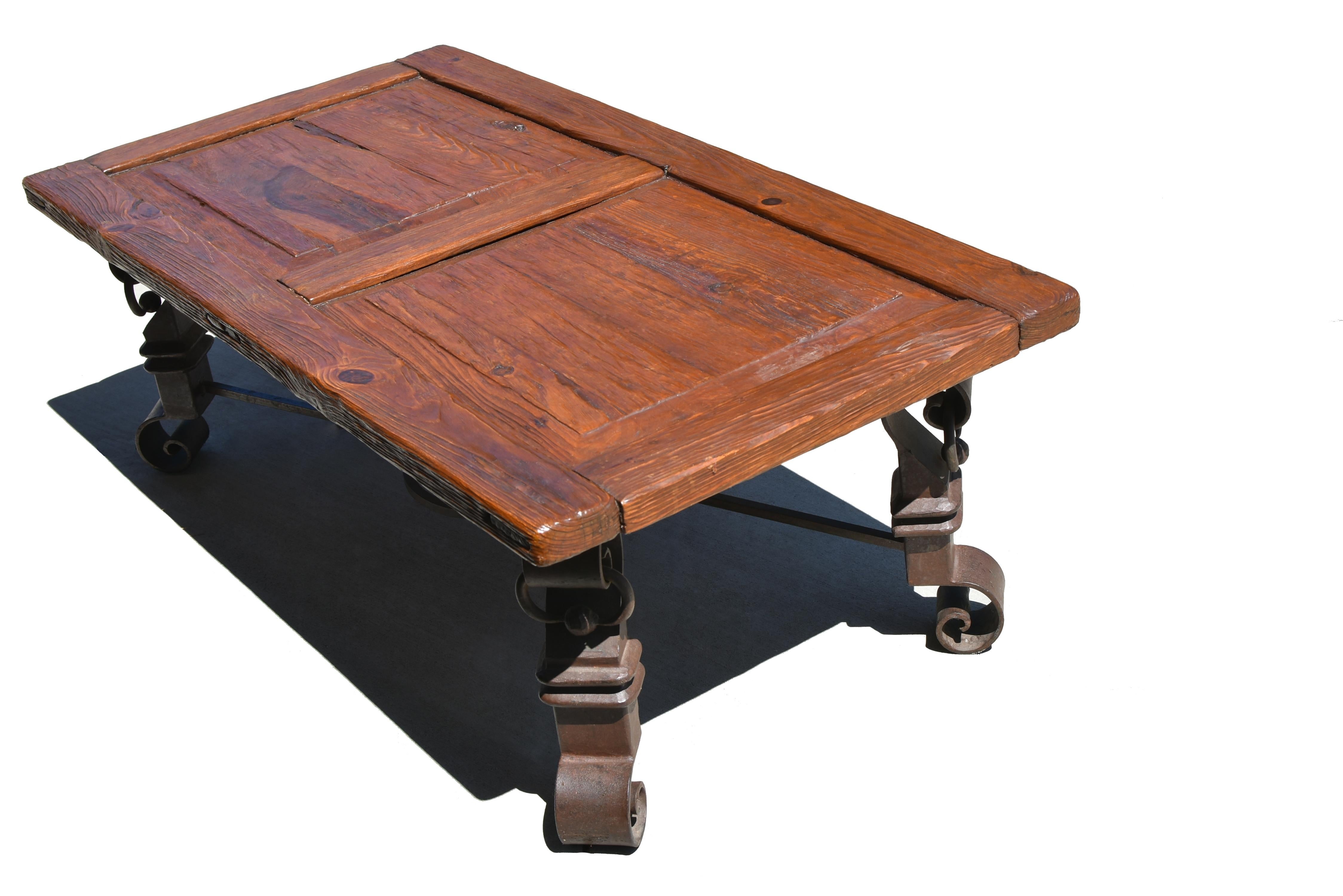 A beautiful antique Spanish Colonial table featuring a repurposed antique wood door as the tabletop, paired with a solid wrought iron base. The bold iron legs are elegantly curved, adorned with substantial rings, and joined at the center by a