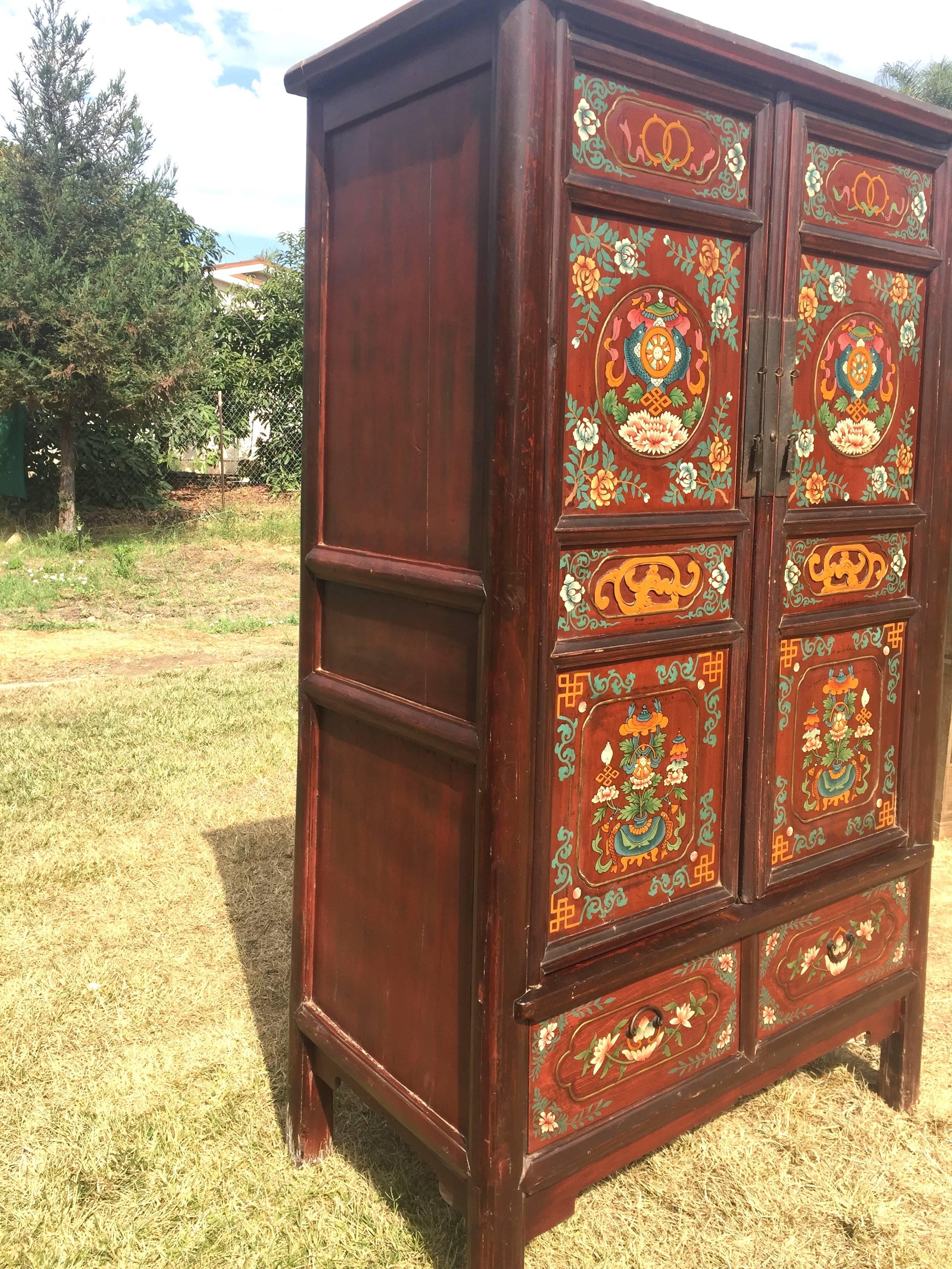 A hand-painted antique Tibetan cabinet. 

This large piece features hand-painted "7 auspicious symbols" in the Tibetan culture. The main areas show umbrella shielded prayer wheels flanked by fish above unity symbols on top of peonies. Such