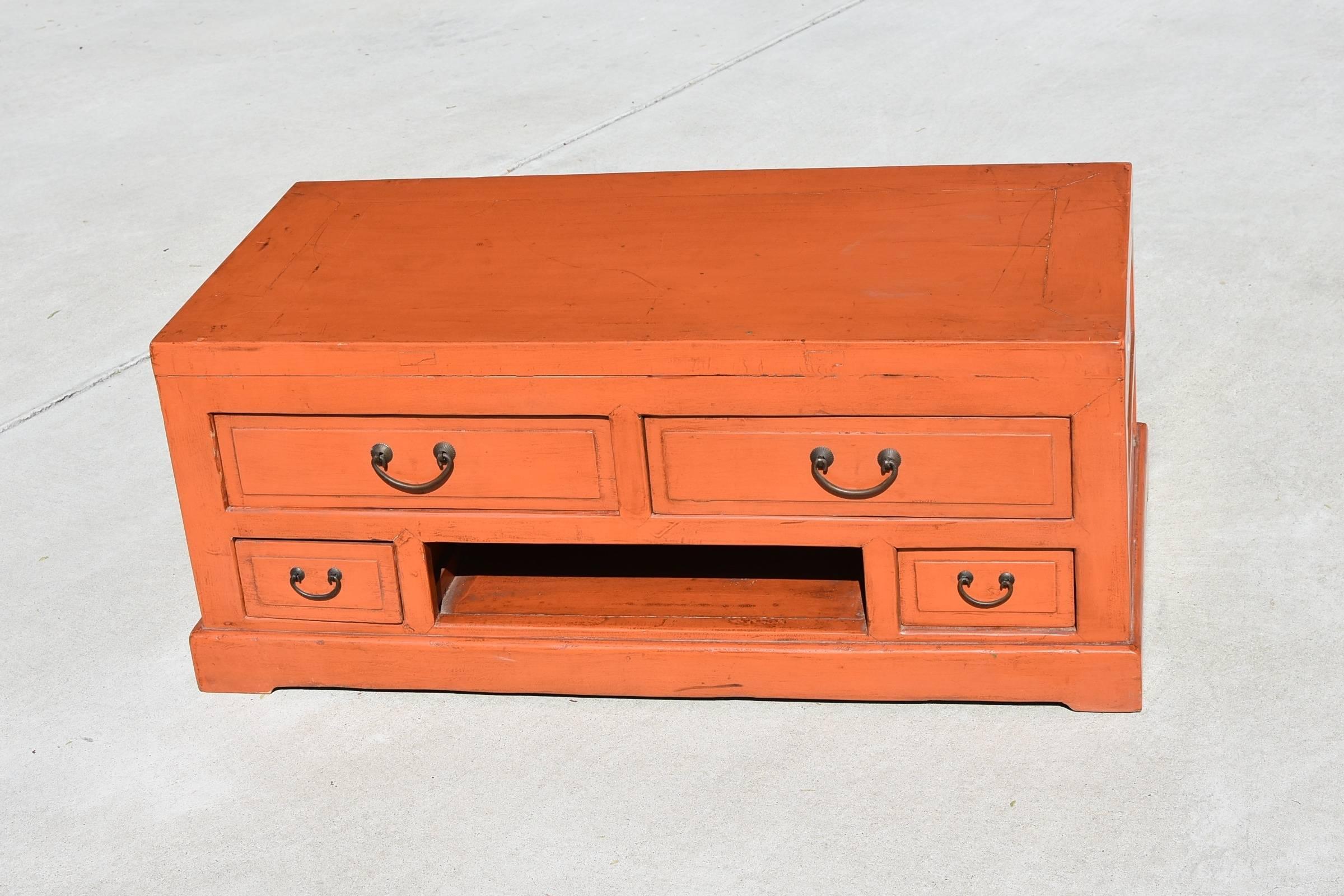 A special low table/chest that is lacquered in the unique color of orange. The solid wood piece has 4 full length drawers and an open space. It makes a great TV stand with cable box tucked away in the opening. The chest is finished all around making