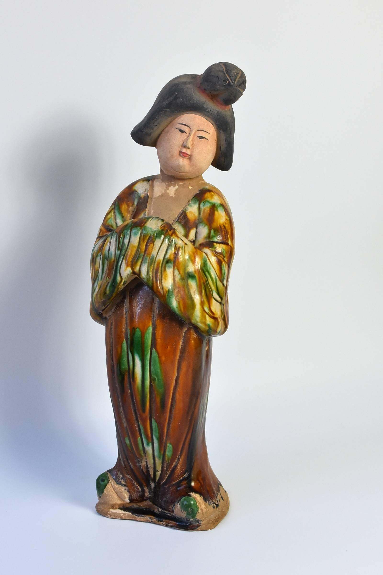 A beautifully made terracotta court lady in the Tang dynasty San Cai style. Fine facial features and traditional dress and hair style. The tri-glaze is the typical green, caramel and beige. The lady's expression is peaceful and serene. Her full face