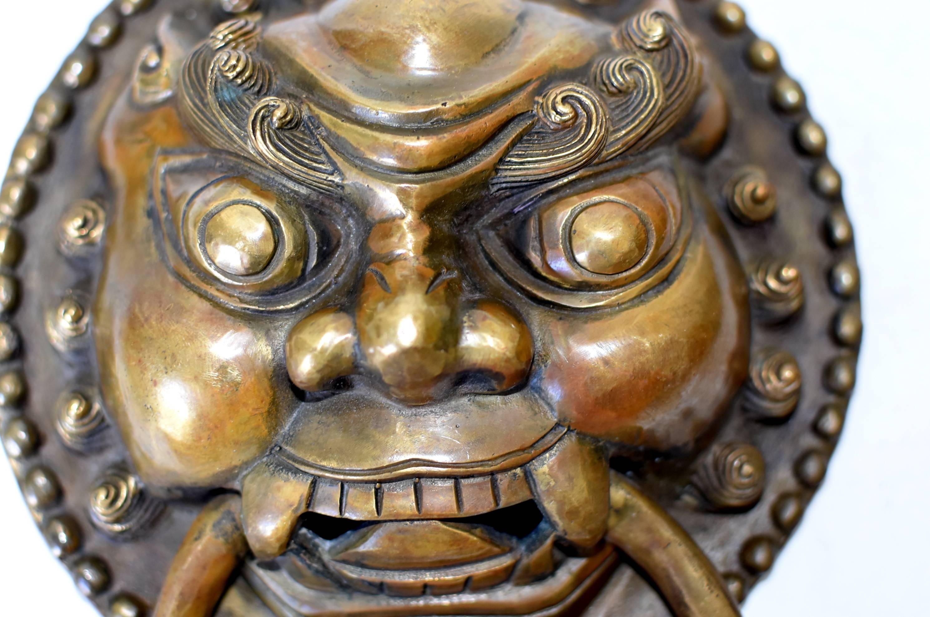 Une paire de magnifiques heurtoirs en bronze à motif de gardien. Le gardien mythique a de grands yeux globuleux au-dessus d'une bouche grande ouverte. Des sourcils forts et bouclés sous un front proéminent. Ses joues rondes et lourdes indiquent