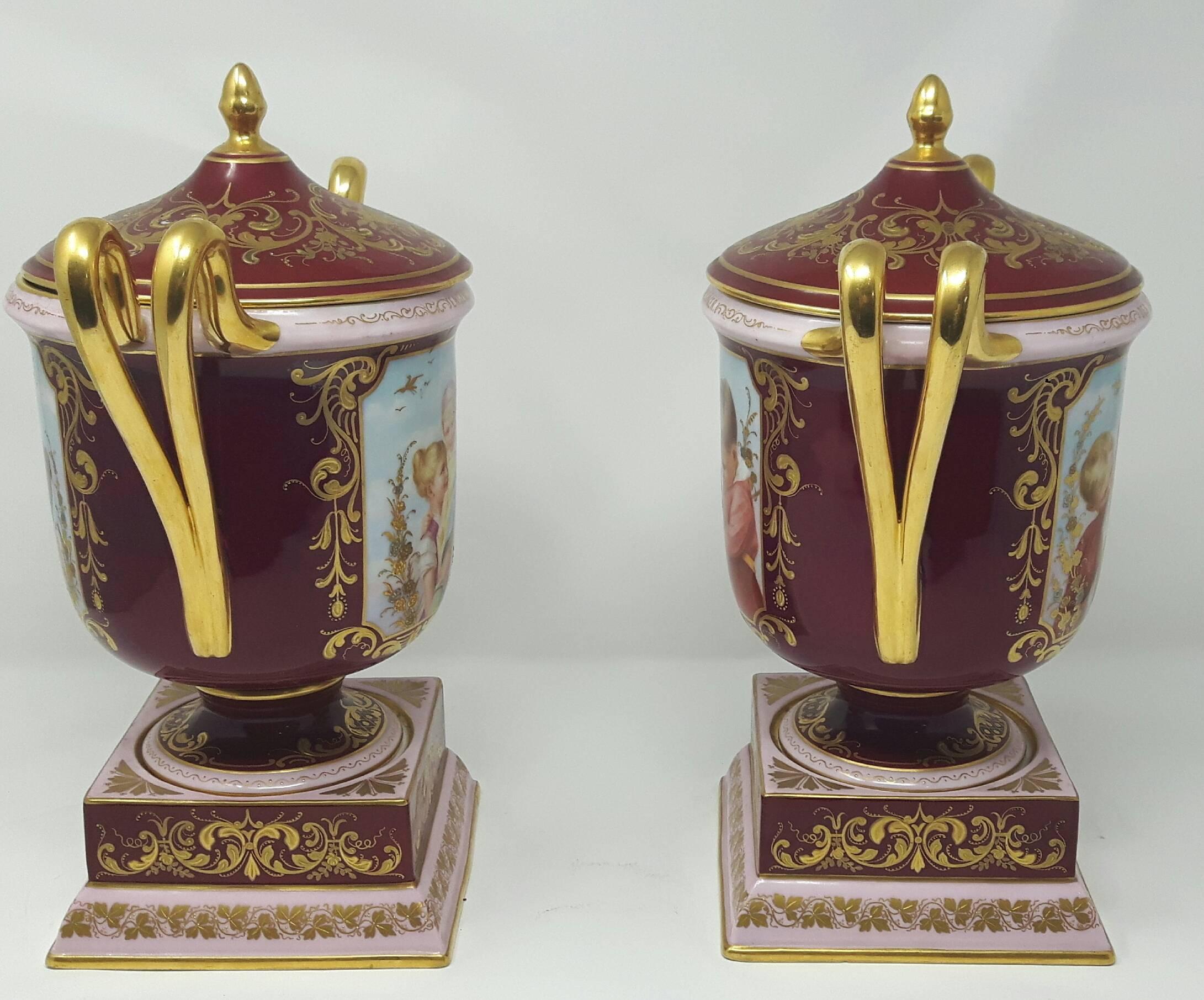 A pair of 19th century vienna vases. Each vase finely painted with two different scenes of children surrounded in gilt borders against a ruby red 
background.
 