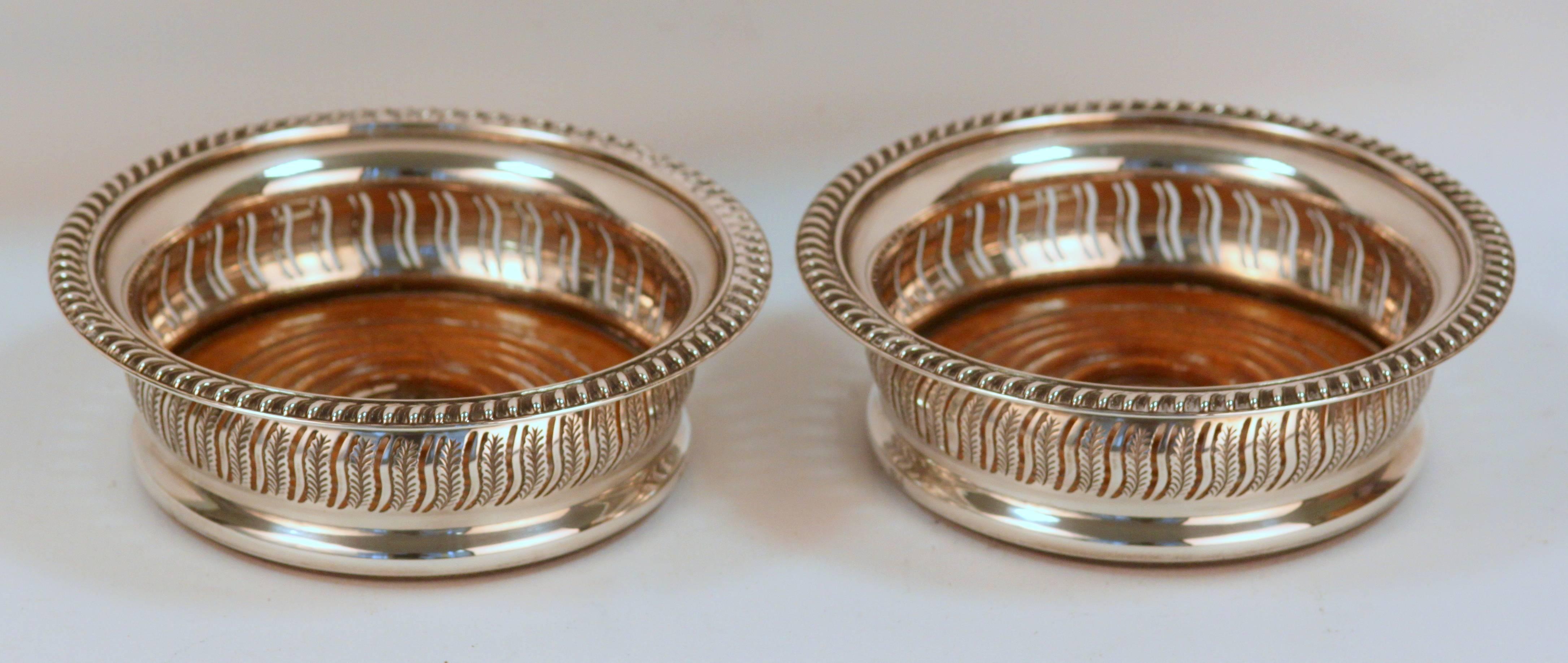 Pair of vintage sterling silver pierced and wooden base wine coasters
Made in Birmingham 1974
Maker: Barker Ellis Silver Co
Fully hallmarked.

Dimensions 
Diameter x height: 14.6 x 4.8 cm
Weight: 395 grams total

Condition: General surface