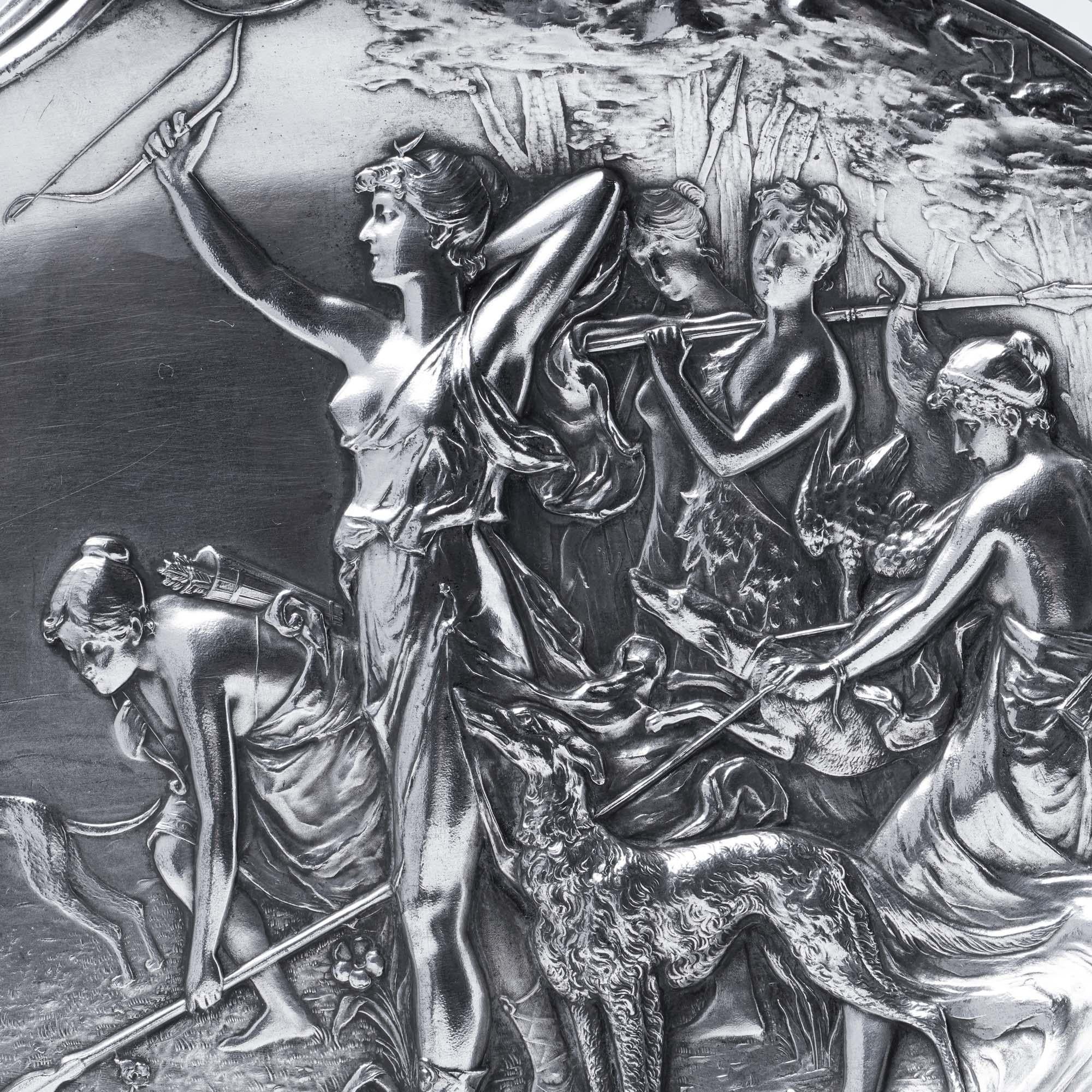 Eine auffällige Jugendstil-Dekorplatte der Württembergischen Metallwarenfabrik (WMF) mit einer fein gegossenen mythologischen Jagdszene in Hochrelief. Das zentrale Motiv zeigt Diana, die Jägerin, umgeben von Nymphen, Hunden und Waldtieren. Die aus