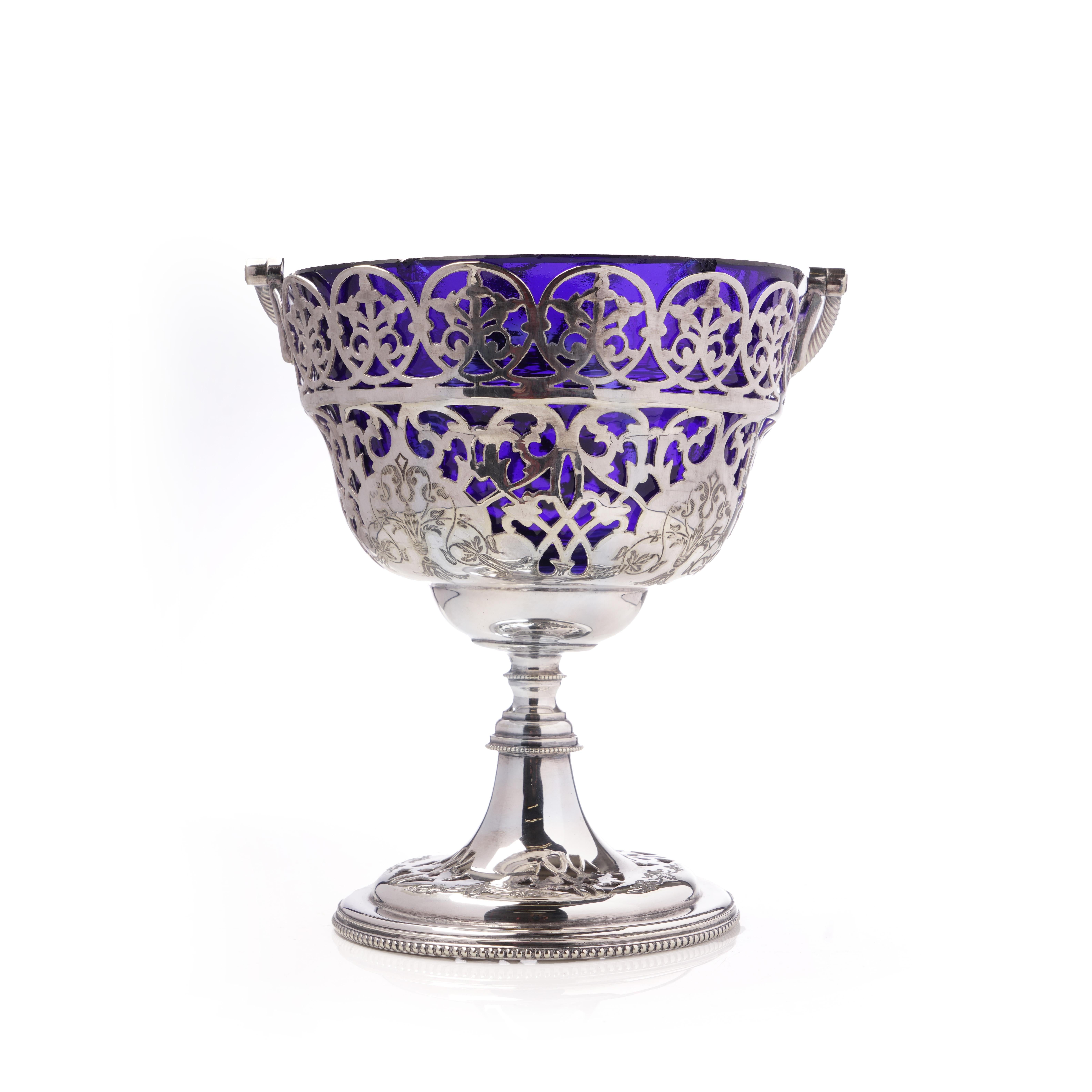 Charmant plat à bonbons en métal argenté de la fin du XIXe siècle ou du début du XXe siècle, orné de motifs floraux et de rinceaux ajourés et d'une doublure en verre bleu cobalt. Le plat repose sur un piédestal aux bords perlés et possède une