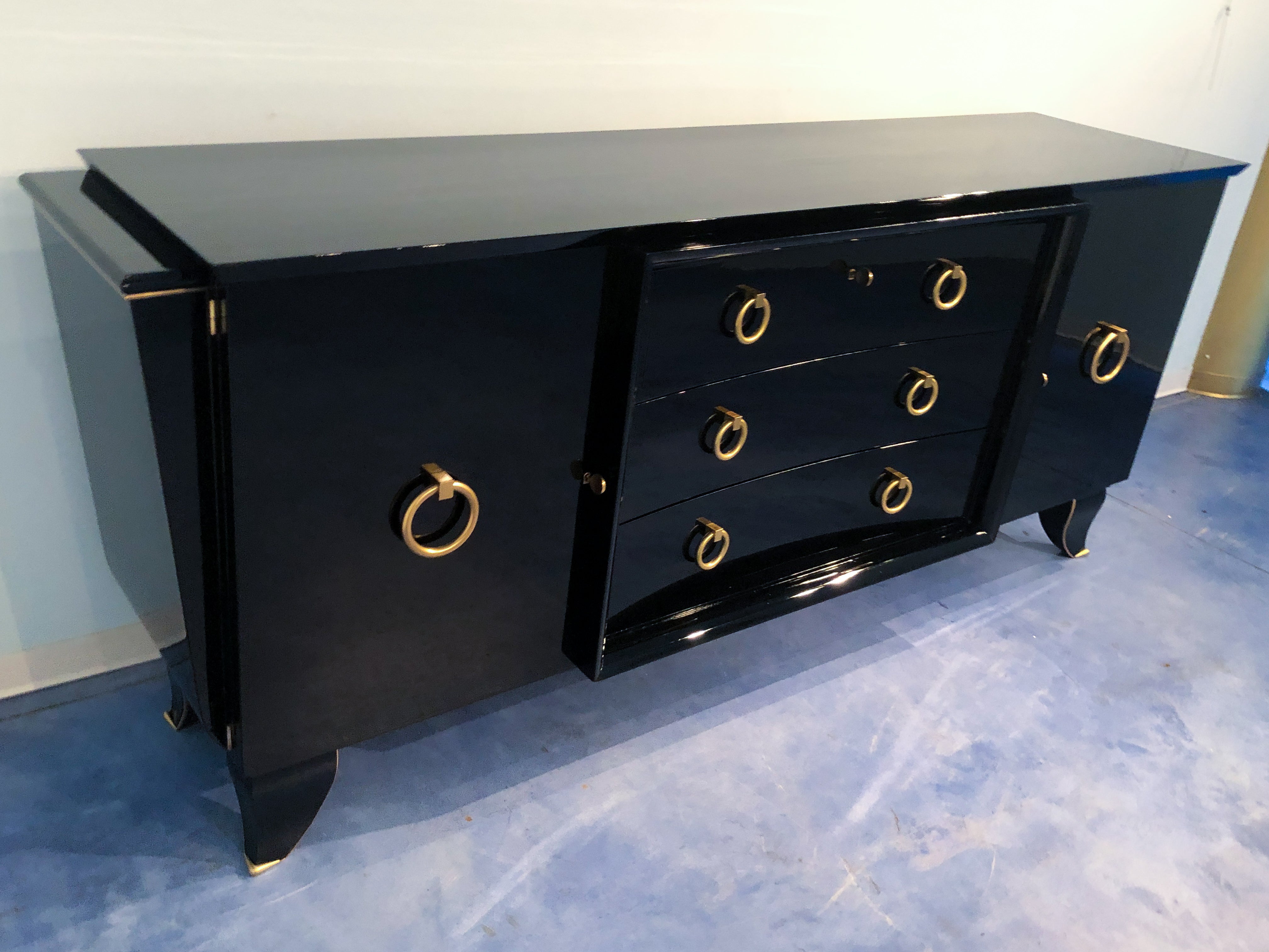 Stylish French Art Deco sideboard in black lacquered mahogany, 1940. The sideboard has a great executive quality, notable in details as jutting sides line, the concave drawers design, original feet shape, and brass decorations. All those details