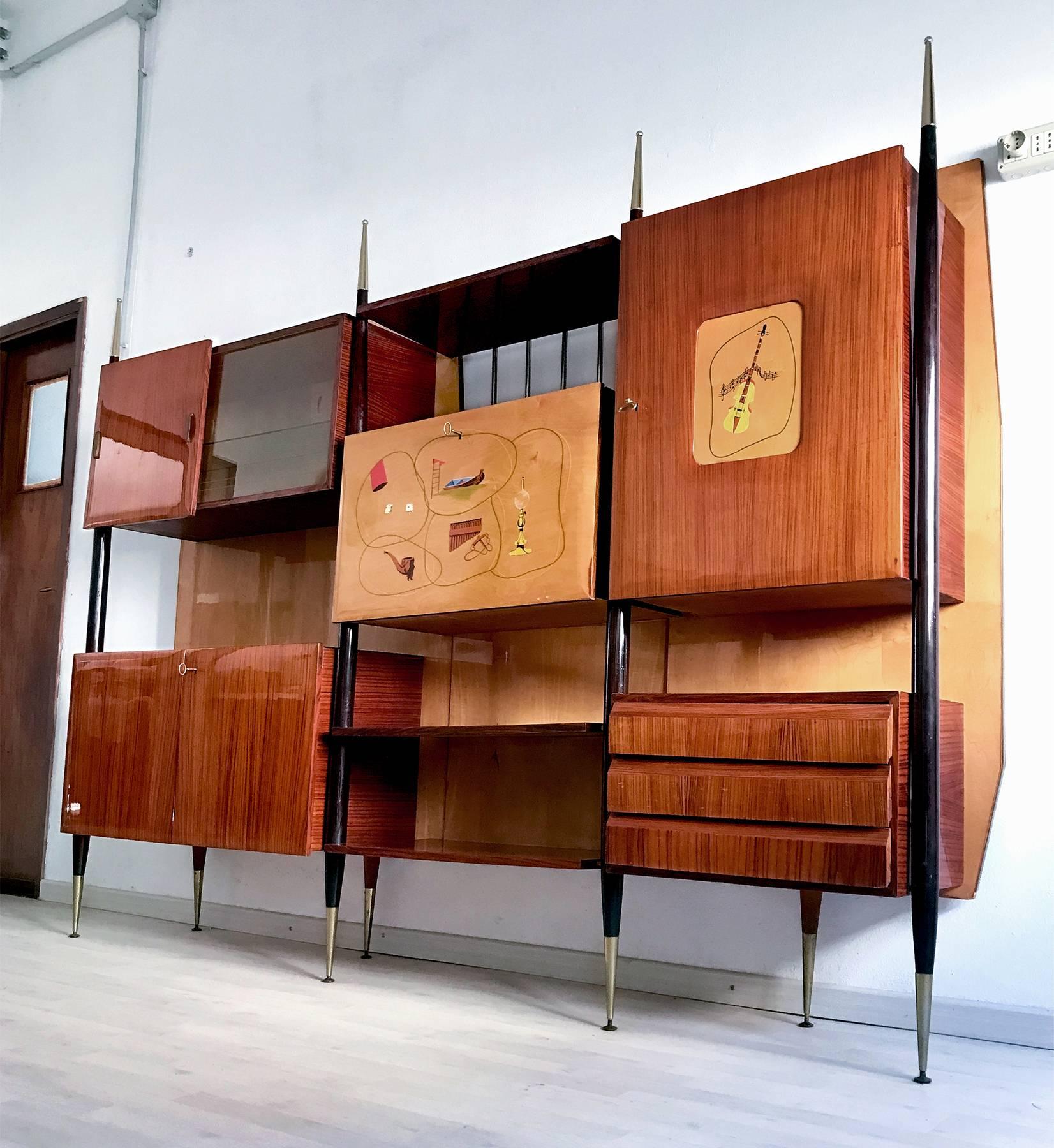 Stunning design for this very rare wall unit of the 1950s structurally supported by four ebonized lances with brass tips, unexpectedly positioned on the front of the structure and absent behind.
It's a multifunctional wall unit, equipped with bar