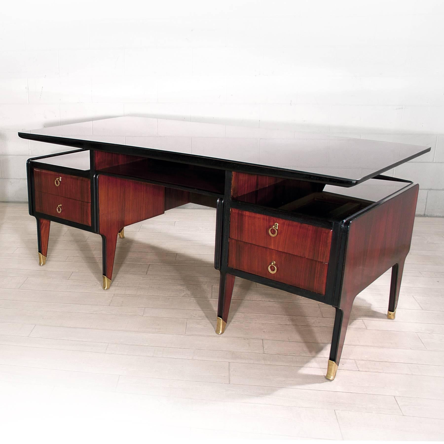 This stylish executive desk has been designed by Vittorio Dassi in the 1950s.
Its structure is rosewood with tapered legs finished with brass sabots, the top table has slightly curved form and is made of black glass, as well as their two side open