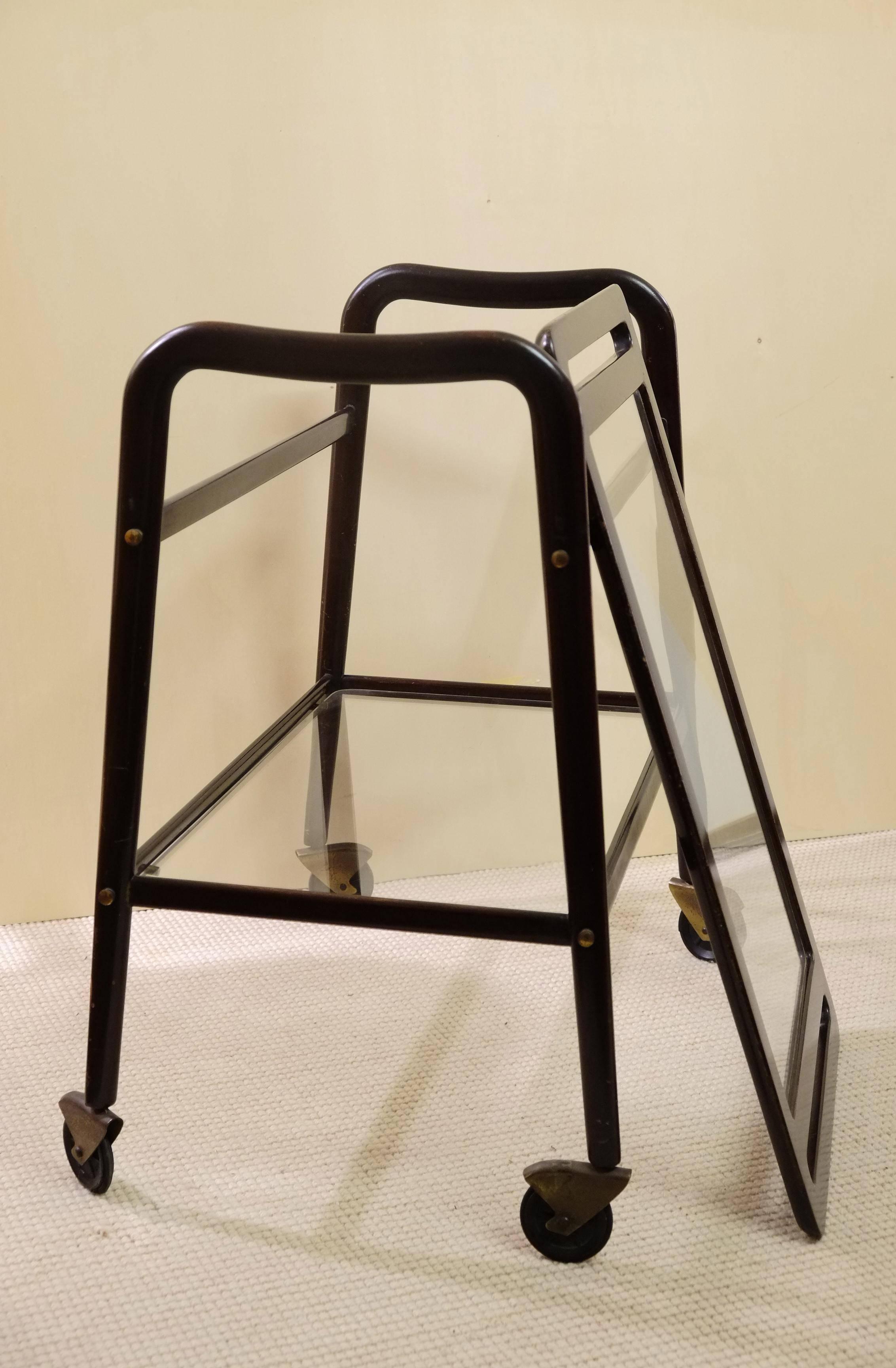 Versatile serving cart designed by Ico Parisi and produced by De Baggis as model no. 60 in 1956. Sculpted black wood frame holds two inset glass shelves. The top shelf lifts off and can be used as a tray. Frame is on casters.