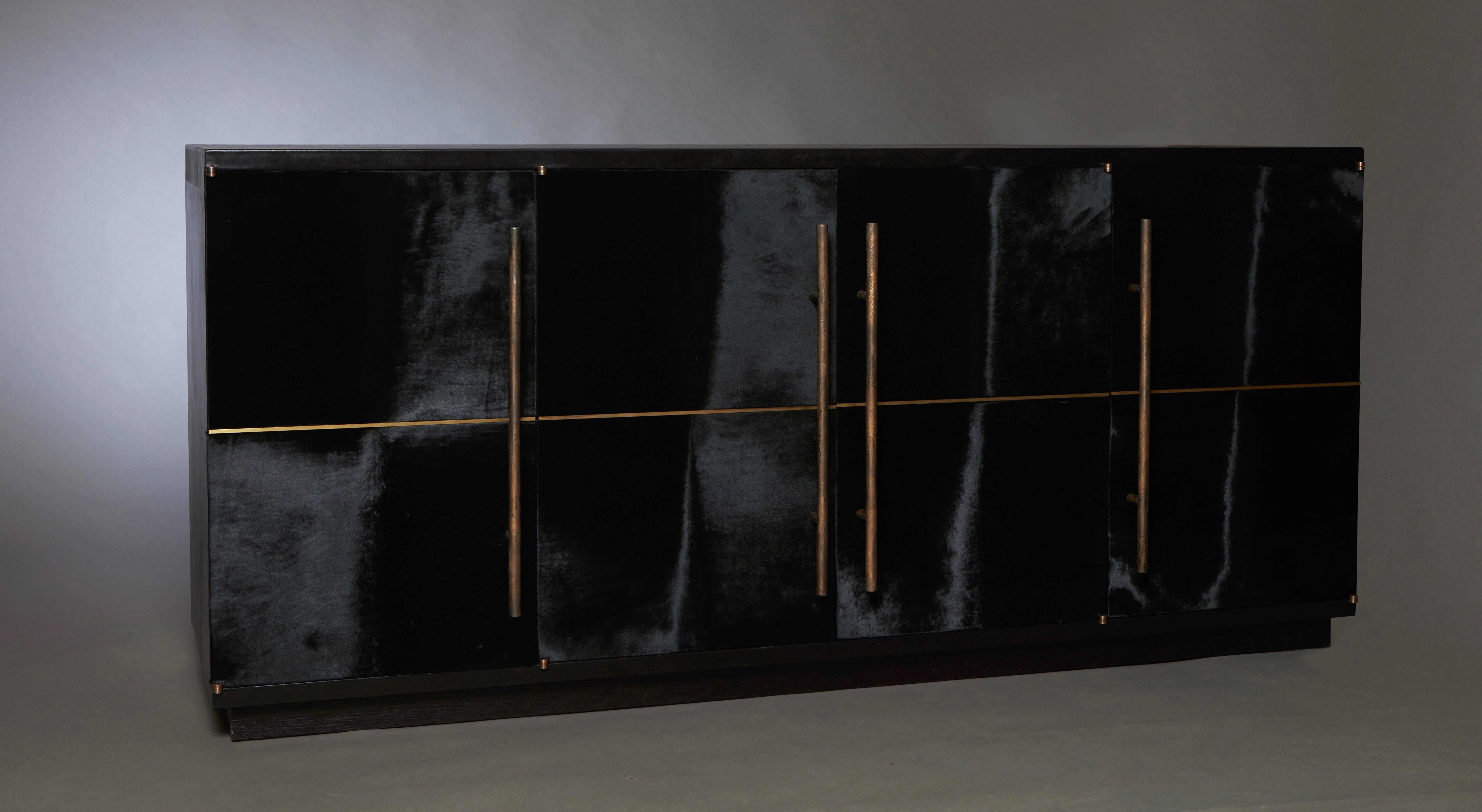 The RAVEN Credenza celebrates the beauty of unpredictable occurrences in natural materials, combined with the artist’s tailored perspective. This all-leather clad piece was built to sit in a regal setting, with its black hair calf doors and forged