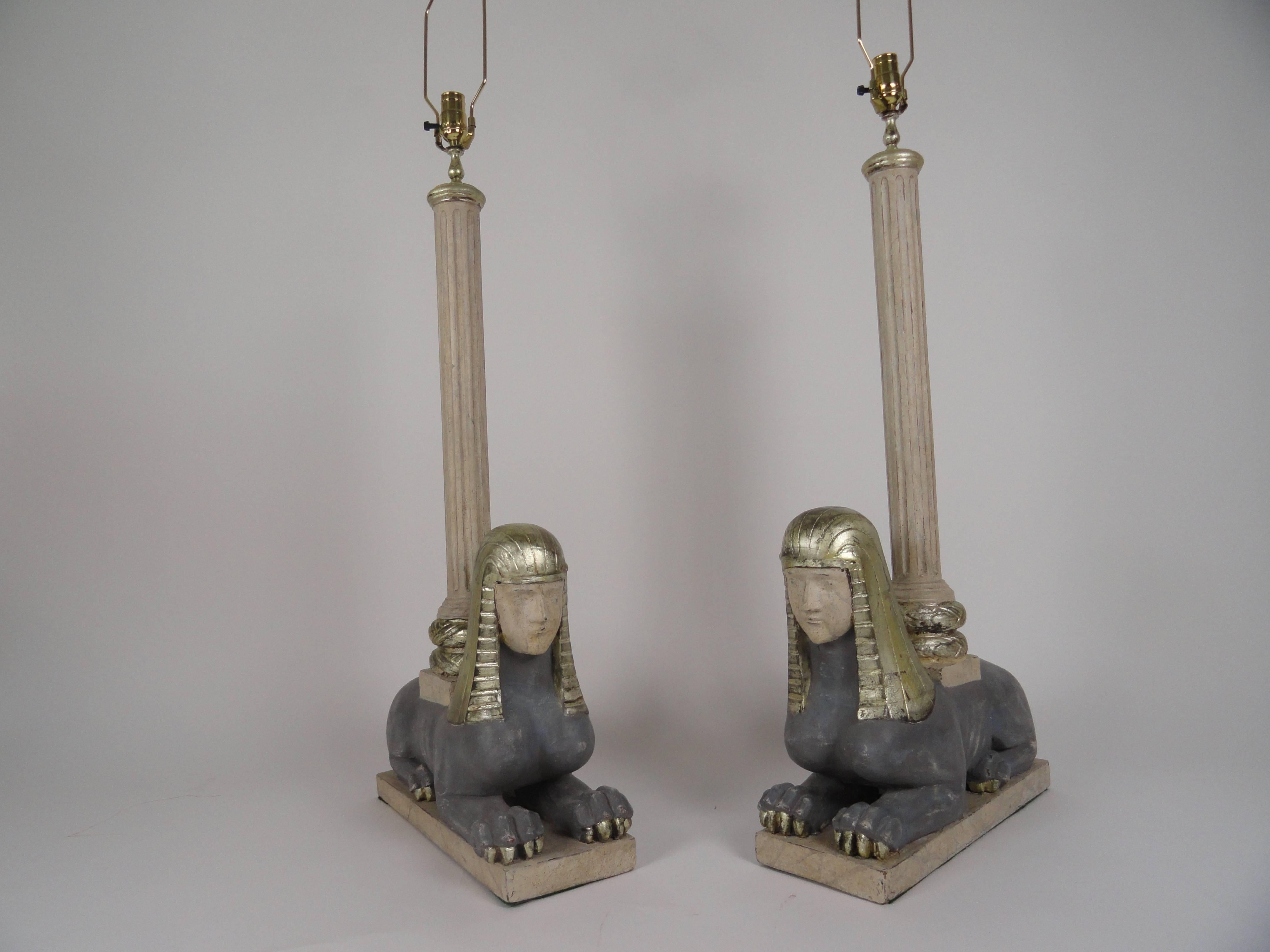 This amazing pair of Bugatti style Egyptian revival fluted column lamps has kneeling Sphinx bases. Pair of Italian lamps in the manner of Bugatti. Carved wood with fluted columns. Newer finish of grays and white gold leaf. Rewired with inline