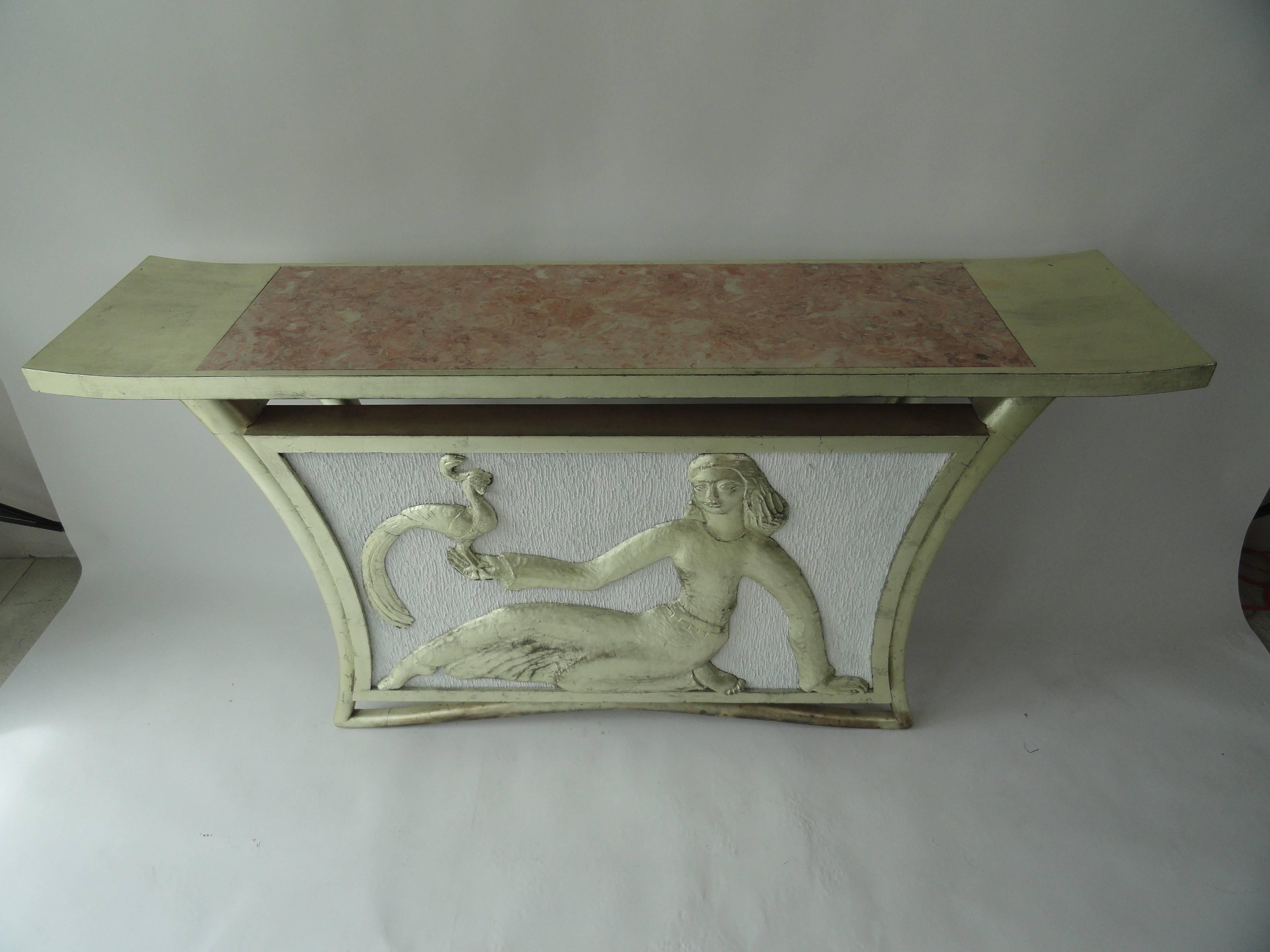 Custom T.H. Robsjohn-Gibbings table with marble inset on top. Carved female figure, Lydia, with peacock. Newer silver leaf finish on frame. White painted fabric background.
Table came from Palm Beach estate.