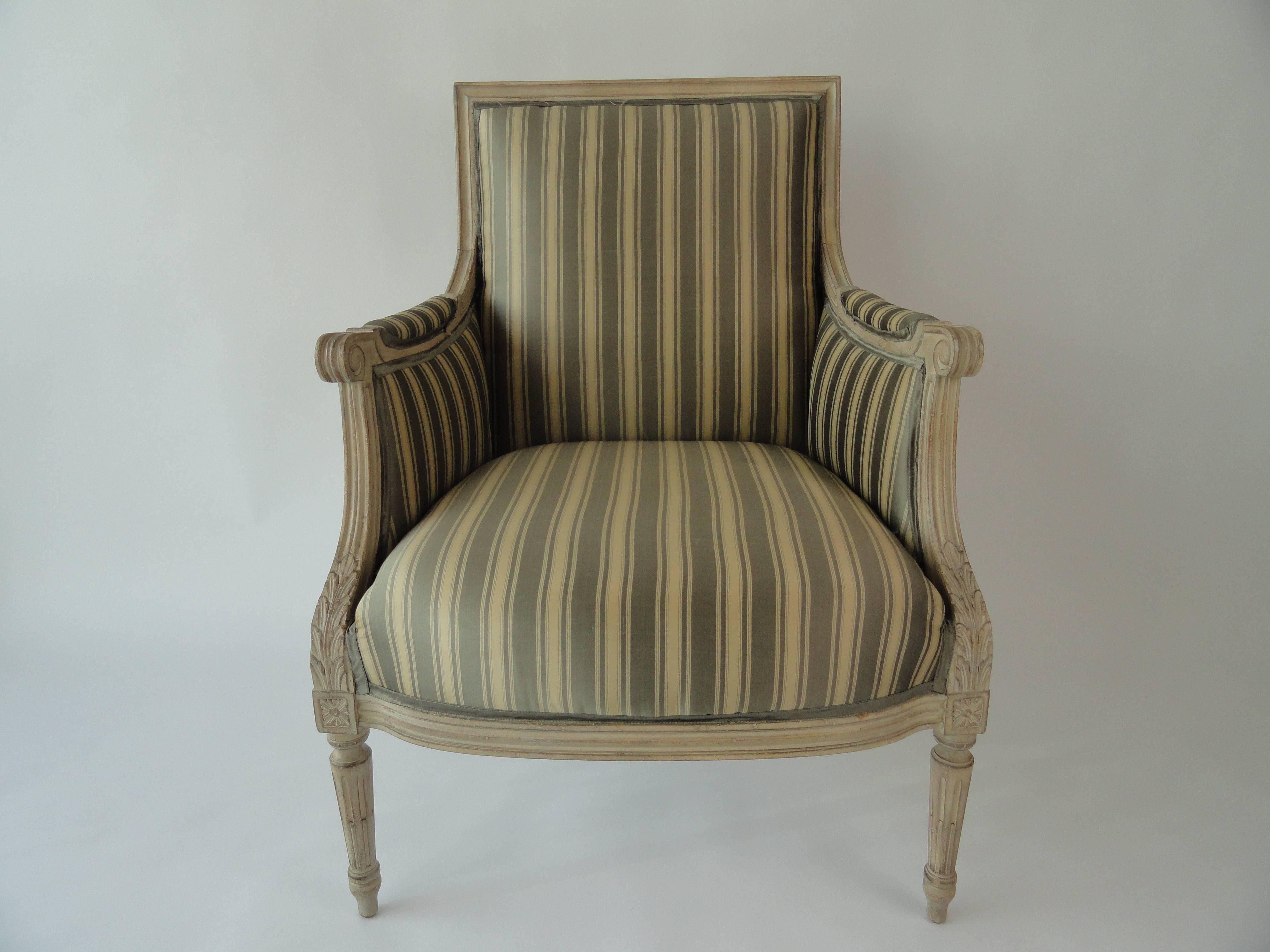 Louis XVI style painted bergere with carved arm detail. Upholstered in gray on beige striped Clarence House silk with silk self-taping.