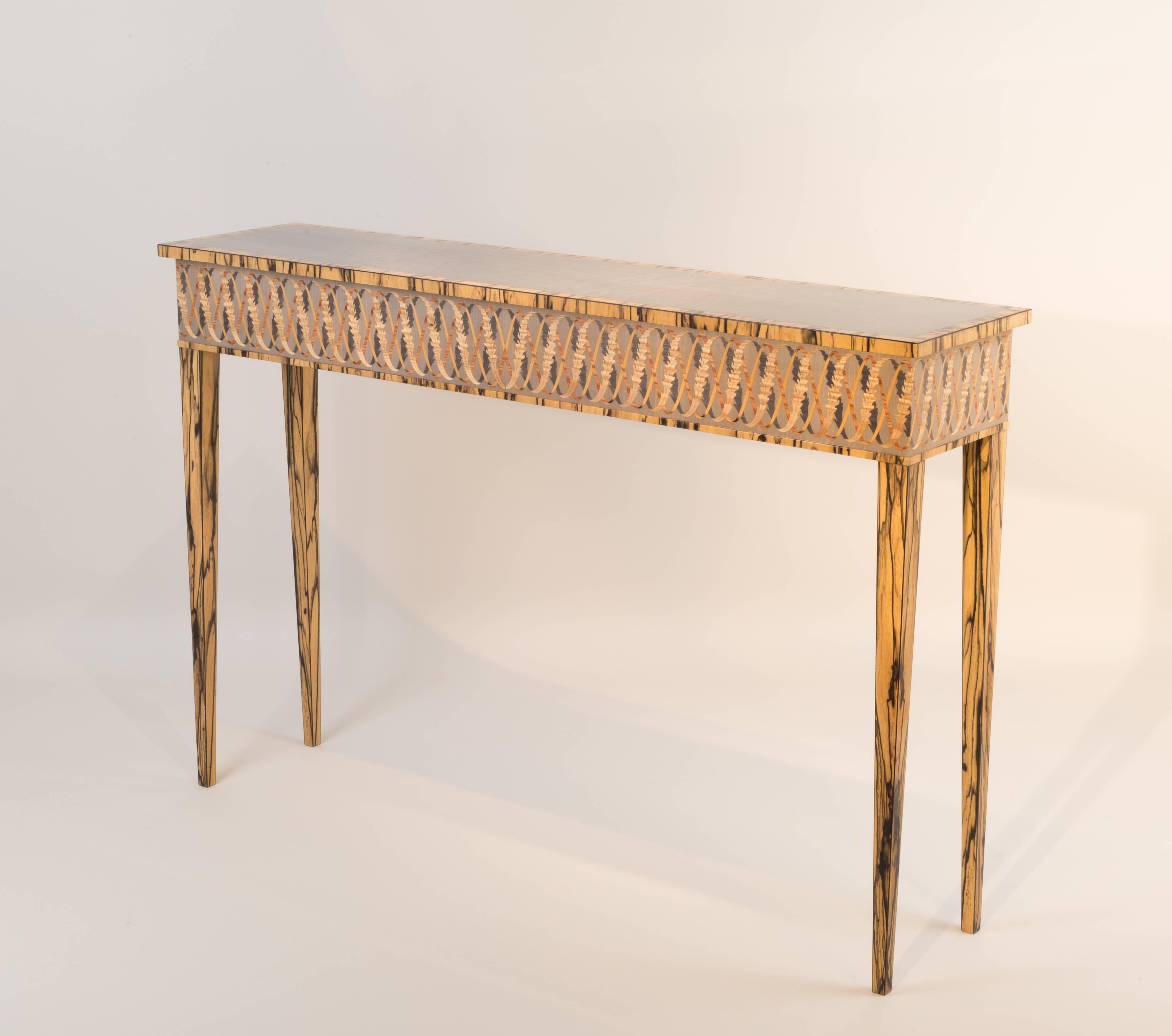 Raised on white ebony veneered legs the frieze helix is inlaid with ash, tulip and boxwood. Italian Sycamore supports the helix and is framed on the top by white ebony.
Ideally placed in a hallway or beneath a mirror this table is designed and